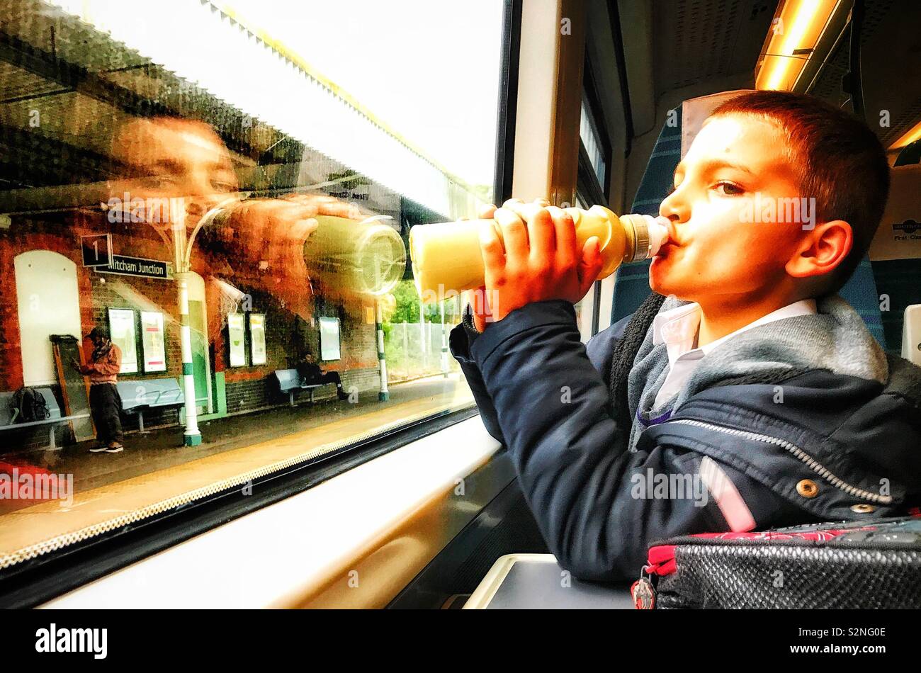 Giovane ragazzo in un treno sorsi da una bottiglia mentre il peering attraverso la finestra del carrello Foto Stock