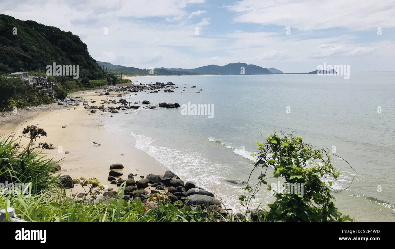 Una spiaggia condito con rocce si protende verso la penisola di montagne. Foto Stock