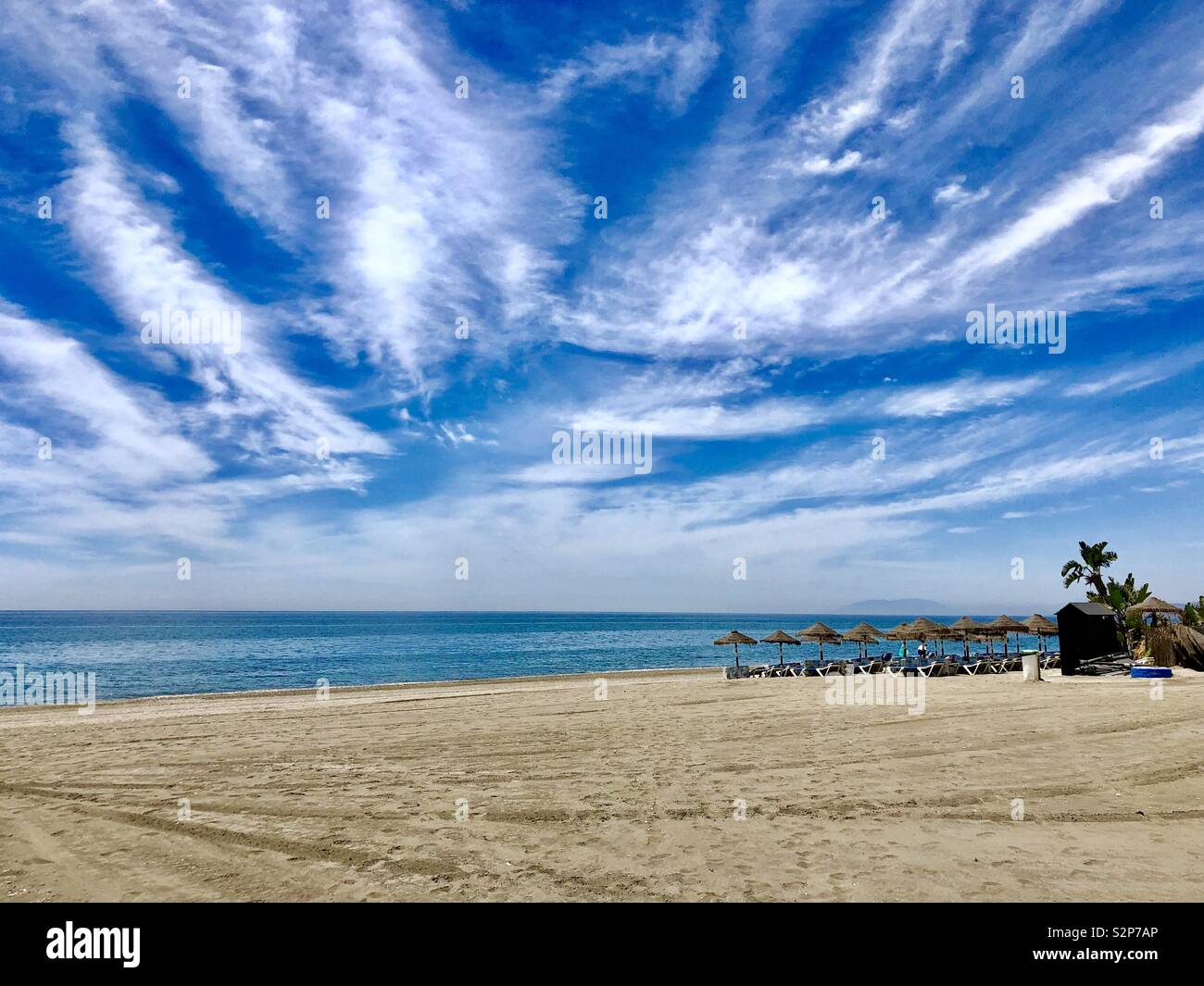 Una scena di spiaggia in Torrox Costa del Sol Spagna mostra profondo cielo blu, la sabbia dorata e il mare blu. Sfumature di spiaggia sono a metà distanza. Foto Stock