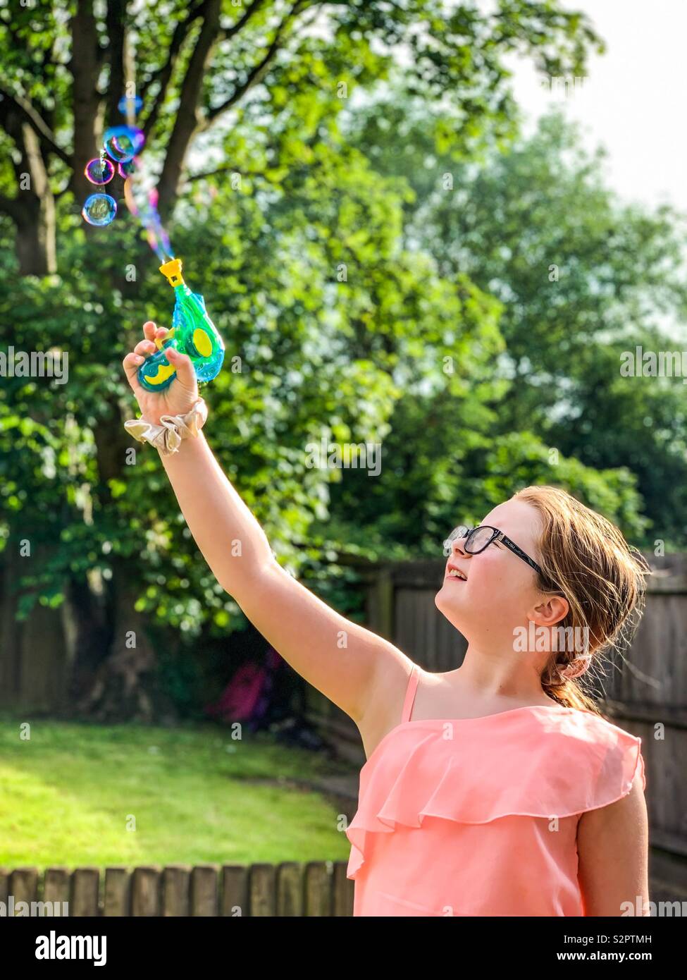 Ragazza giovane soffiare bolle con una pistola giocattolo in giardino Foto Stock