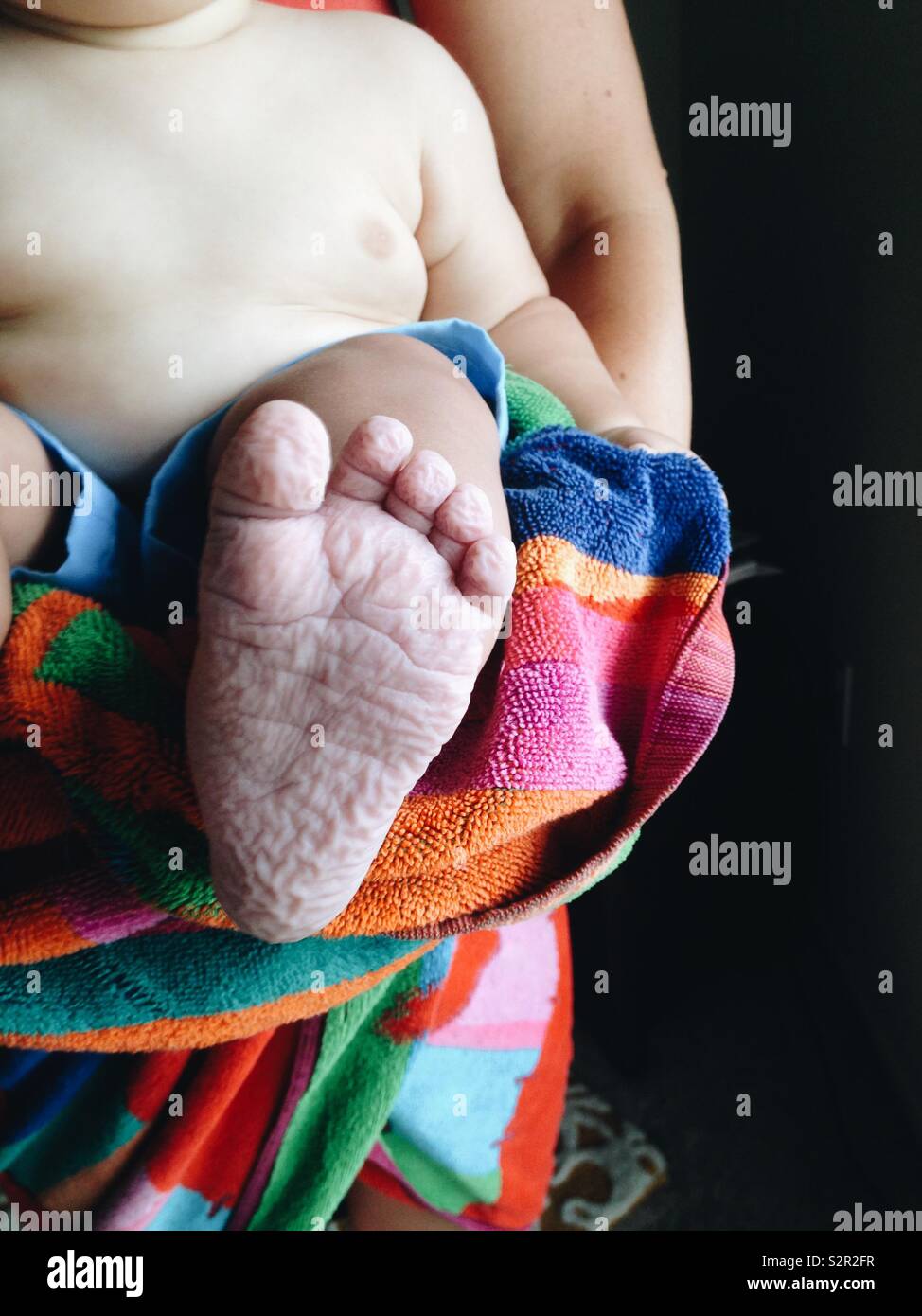 Il fondo di un bambino rugoso piede dopo il nuoto con il bambino che si terrà in mom di braccia con un colorato telo da spiaggia. Foto Stock