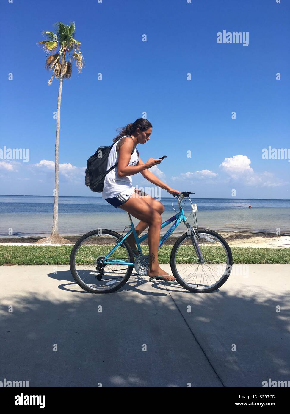 Donna in bici tramite telefono cellulare mentre pedalando attraverso un albero di palma Foto Stock