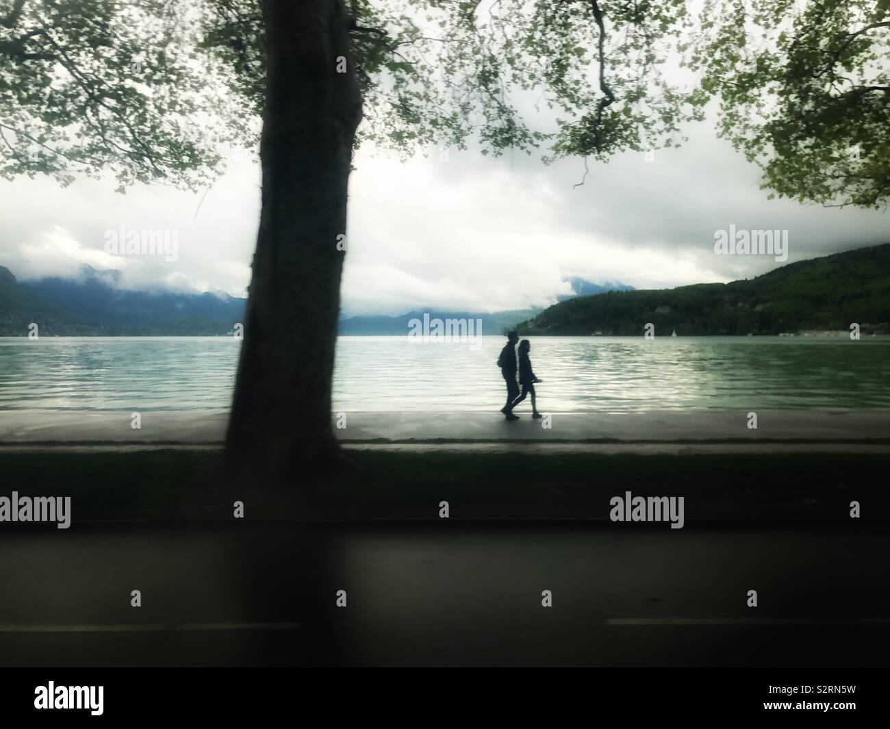 Silhouette di un giovane a piedi dal lago di Annecy sotto in un giorno di pioggia in primavera , Francia Europa Foto Stock