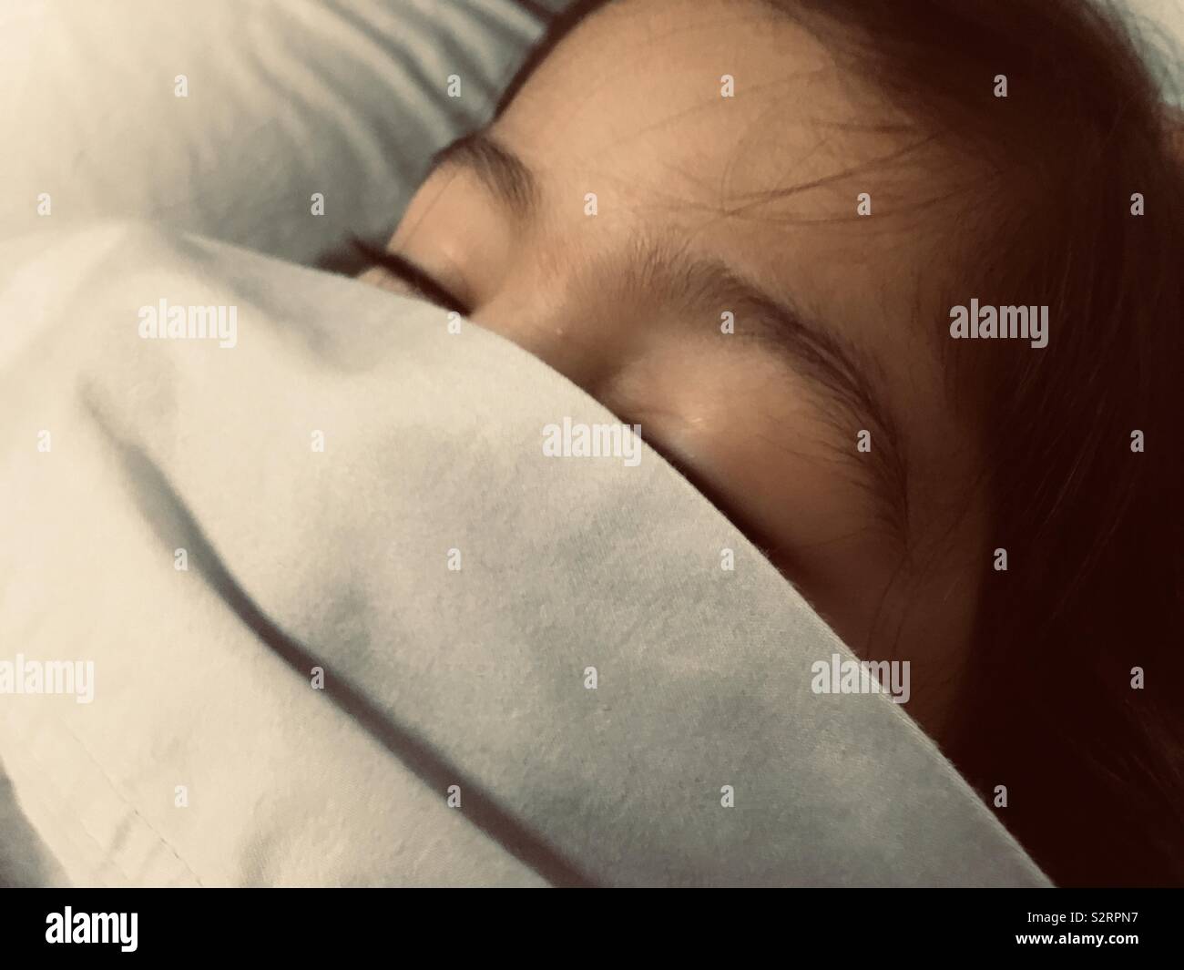 Una vista ingrandita di un'estate cotone lenzuolo che copre un giovane multi-etnico ragazza in bocca e naso. Foto Stock