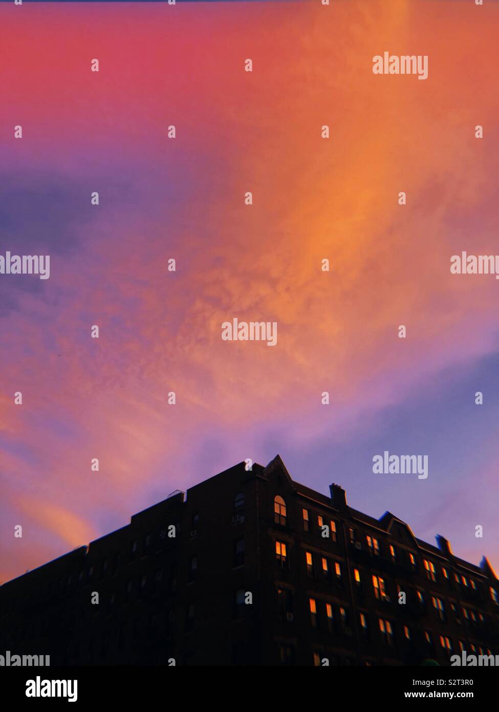 Un intriso di colore rosa, viola e arancione tramonto sopra la parte superiore di un edificio stagliano con luminose finestre Foto Stock