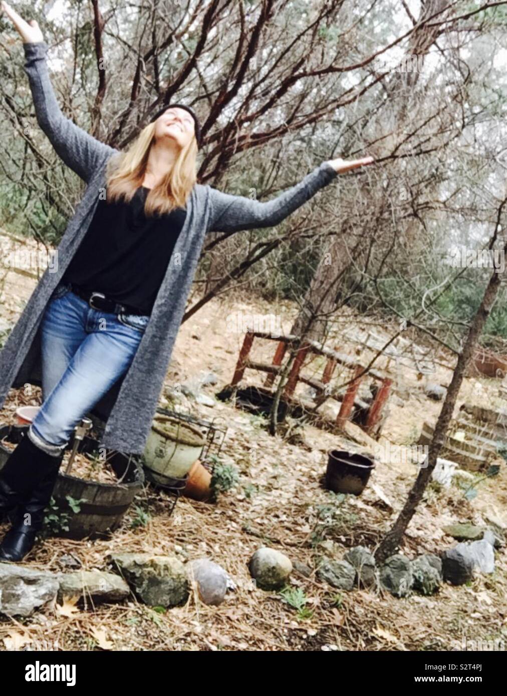 Donna bionda in jeans e stivali, piedi tra alberi nudo durante l'autunno,  inverno in natura con le braccia in aria, sorridente Foto stock - Alamy