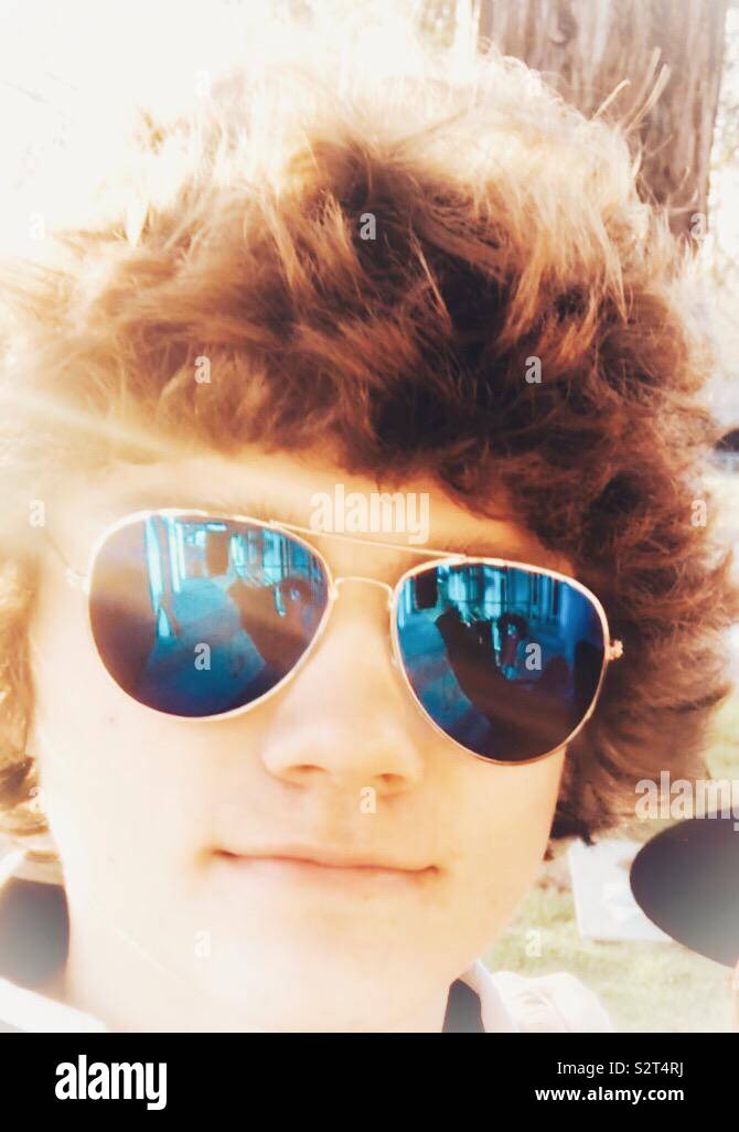 Ragazzo adolescente indossando occhiali da sole aviatore che riflettono con capelli selvaggi mentre sorridente Foto Stock