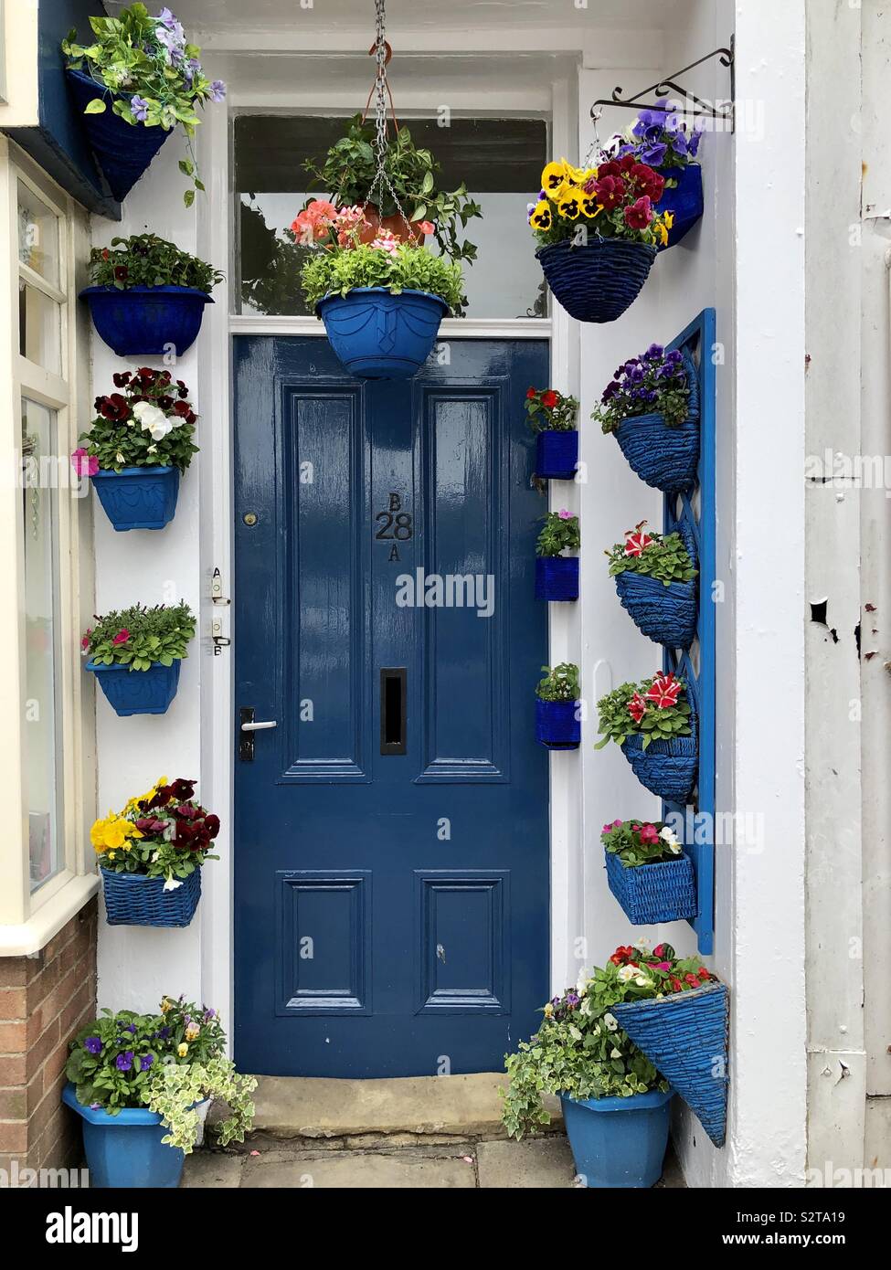 Porta blu in un portico circondato da fiori in blu piantatrici e pentole Foto Stock