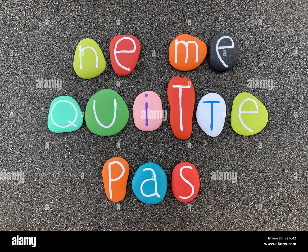 Ne me quitte pas, non lasciare me, frase in francese composta con pietre multicolore su sabbia nera vulcanica Foto Stock