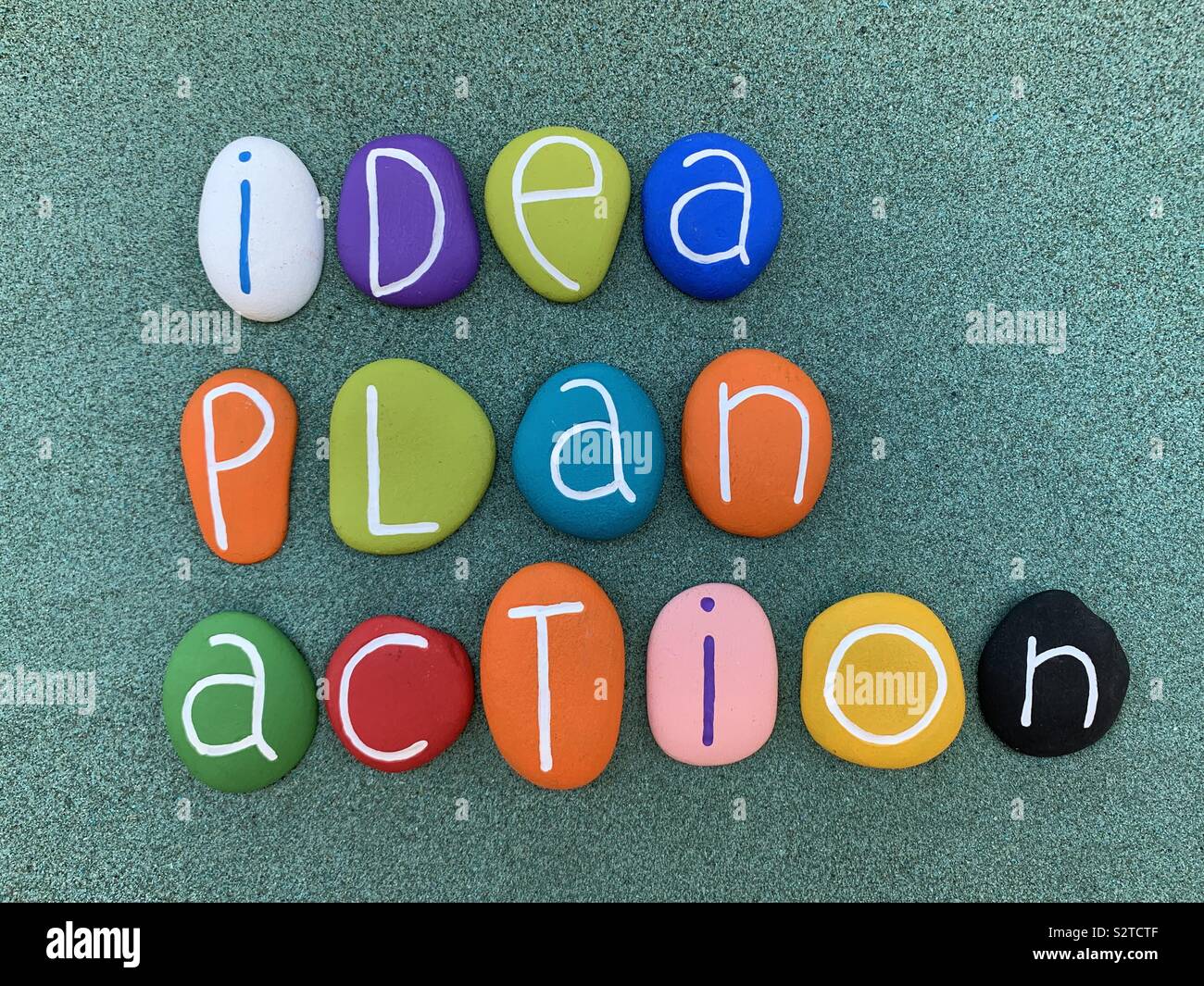 Idea, il piano di azione, pietra multicolore lettere composizione sulla sabbia verde Foto Stock