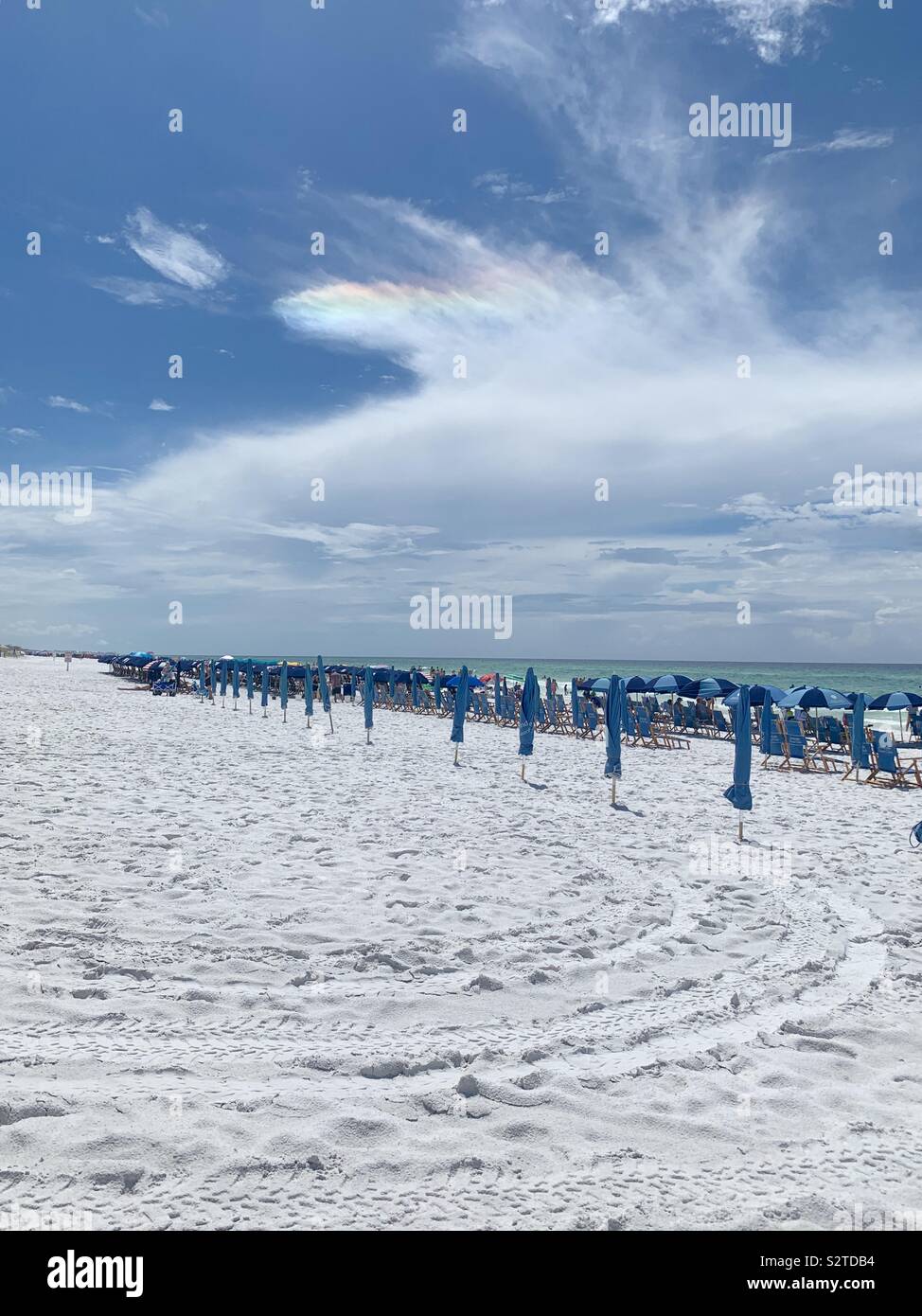 Spiaggia di sabbia bianca con arcobaleno nel cielo e la fila di ombrelloni blu con vista oceano Foto Stock
