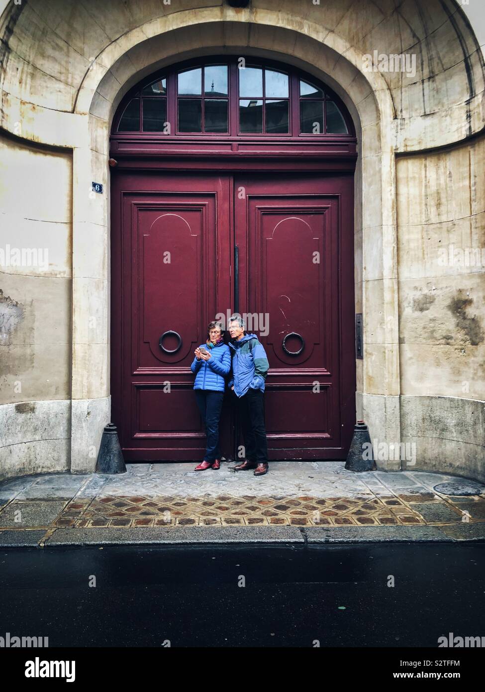 Coppia di mezza età guardando i loro telefoni accanto a una vecchia porta di Parigi Foto Stock