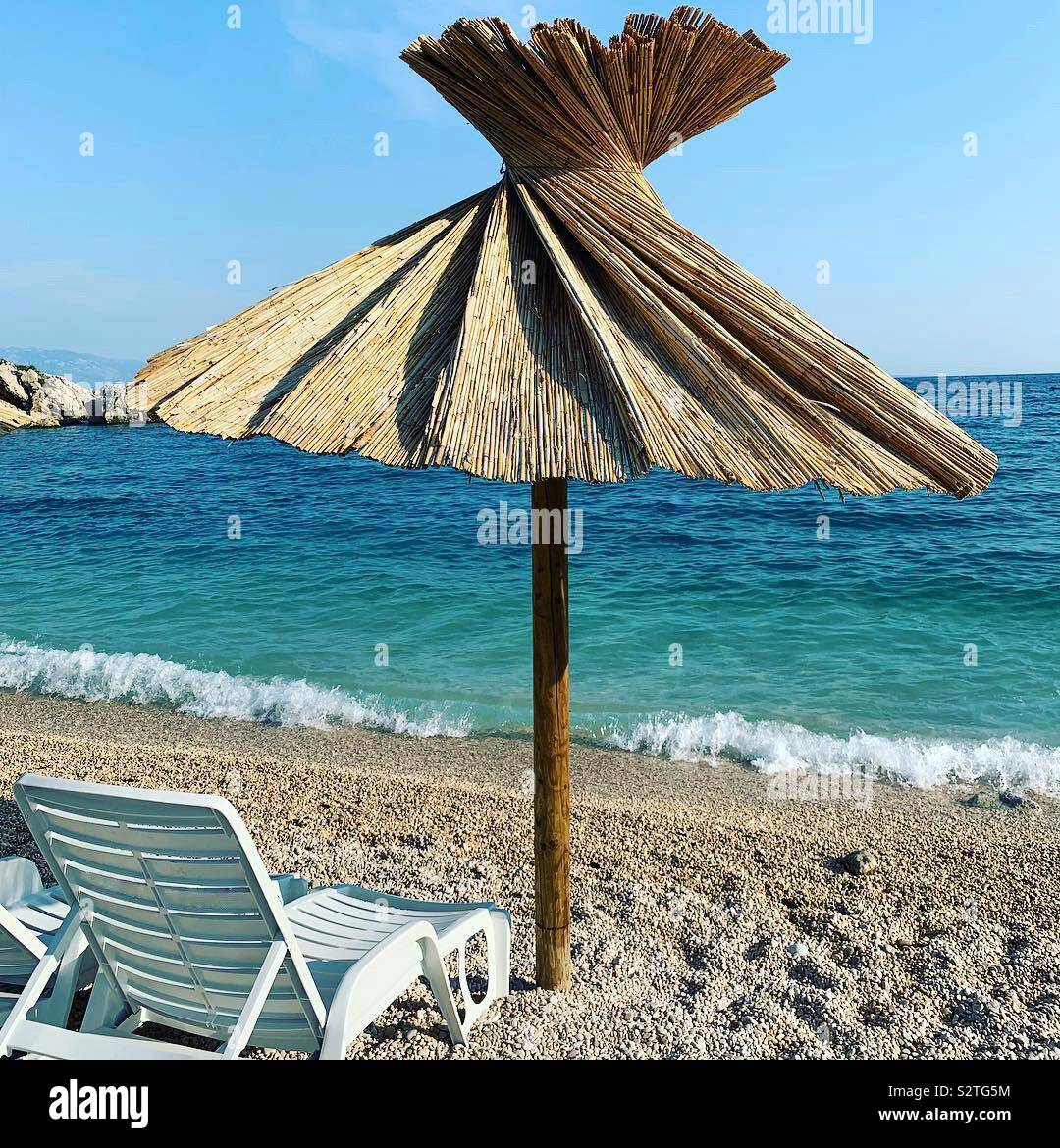 Chaise longue e paglia ombrellone sulla spiaggia Oprna, Stara Baska Croazia. - Immagine stock catturata con smartphone