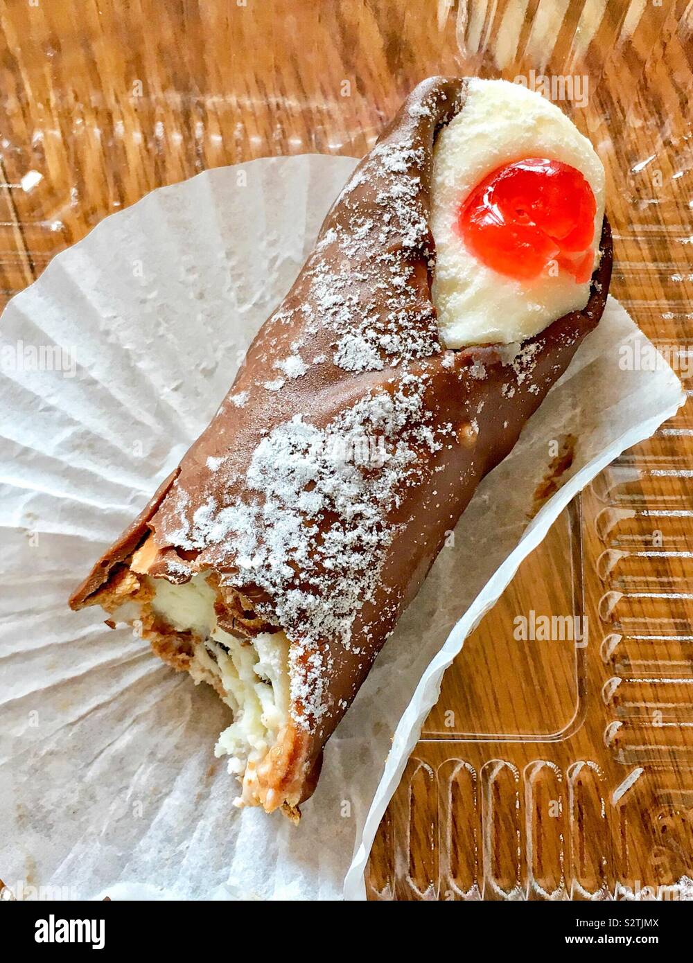 Il cioccolato immerso cannoli con crema dolce ripieno di formaggio, ciliegia candita, spolverato con zucchero a velo in un involucro bianco e contenitore in plastica - Immagine stock catturata con smartphone