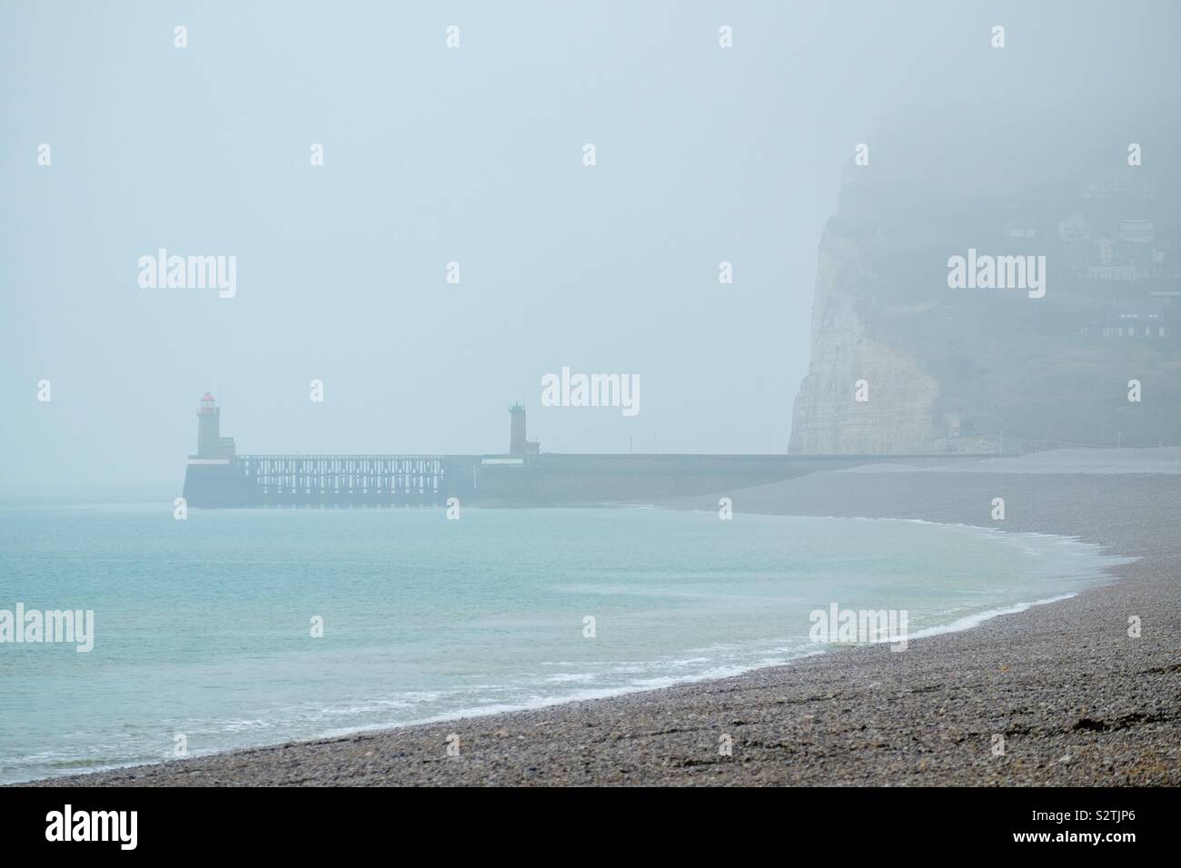 Fécamp, Normandia la spiaggia con le bianche rocce di gesso su una grigia giornata di nebbia che mostra i fari del porto di la distanza Foto Stock