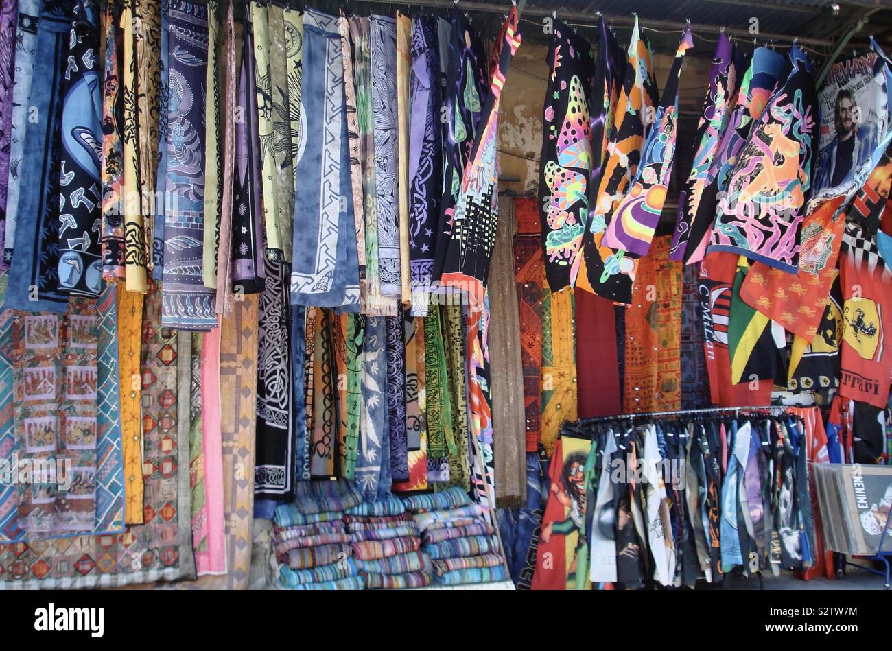 Commerciante di strada nel centro storico di Atene, Grecia, vendendo i colori vivaci dei tessuti, magliette e bandiere. Questo è stato di fronte i resti della biblioteca di Adriano in Areos Street. Foto Stock