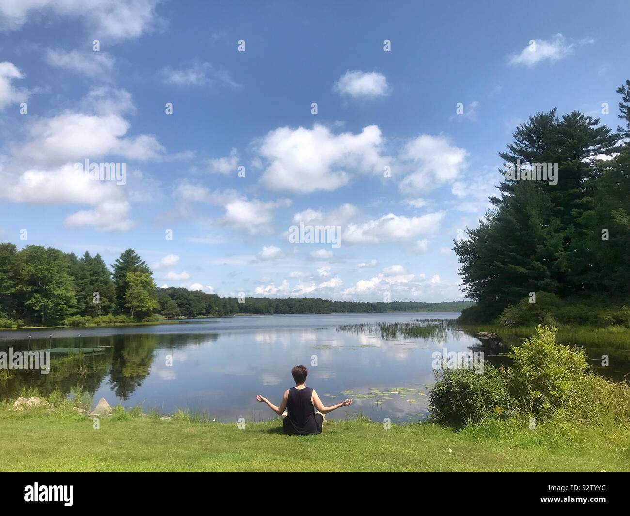 Donna meditando all'esterno da un placido lago Foto Stock