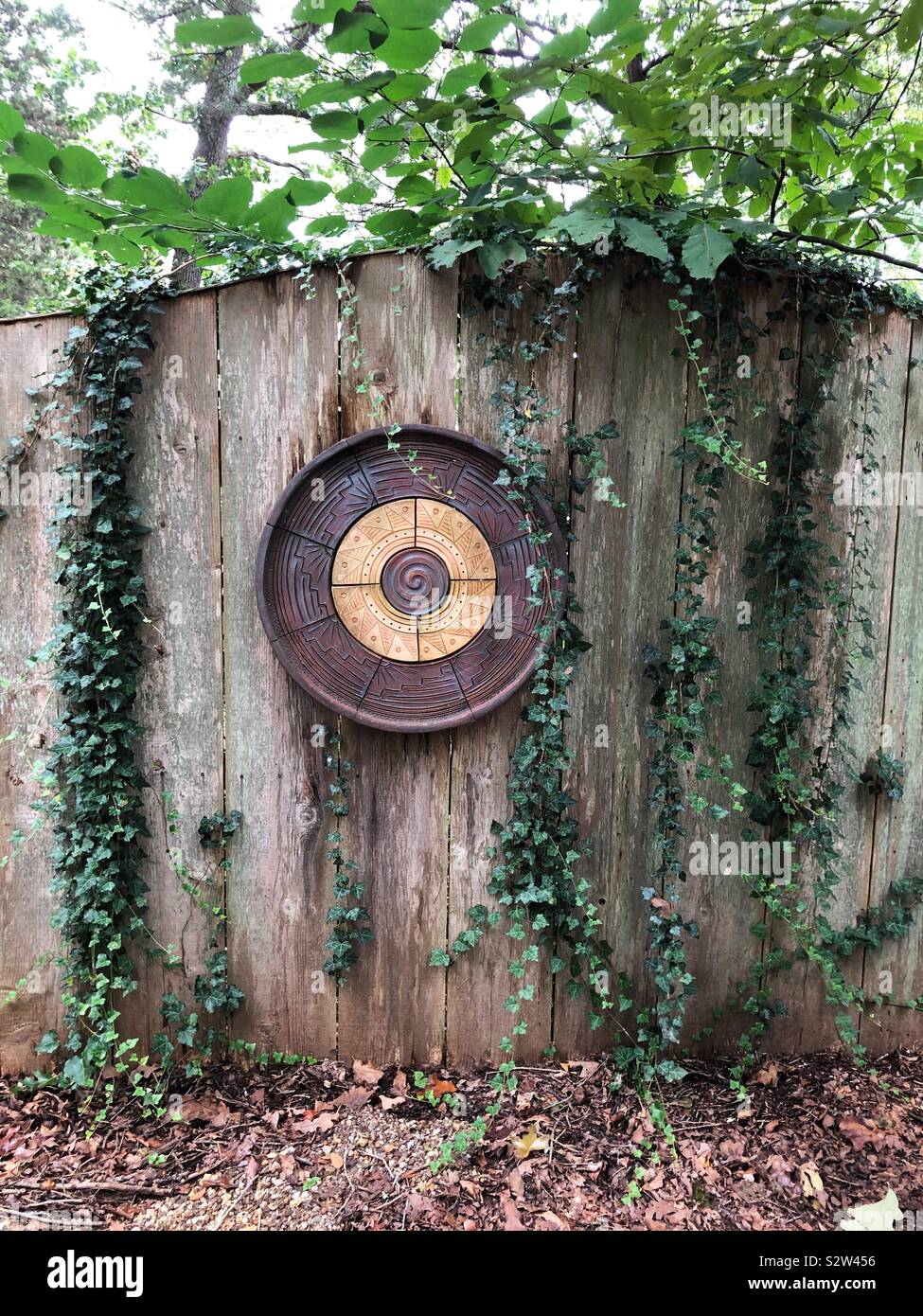 Una staccionata in legno con vitigni e un round scultura in ceramica a terra Studios di Fayetteville, Arkansas, Stati Uniti d'America. Foto Stock