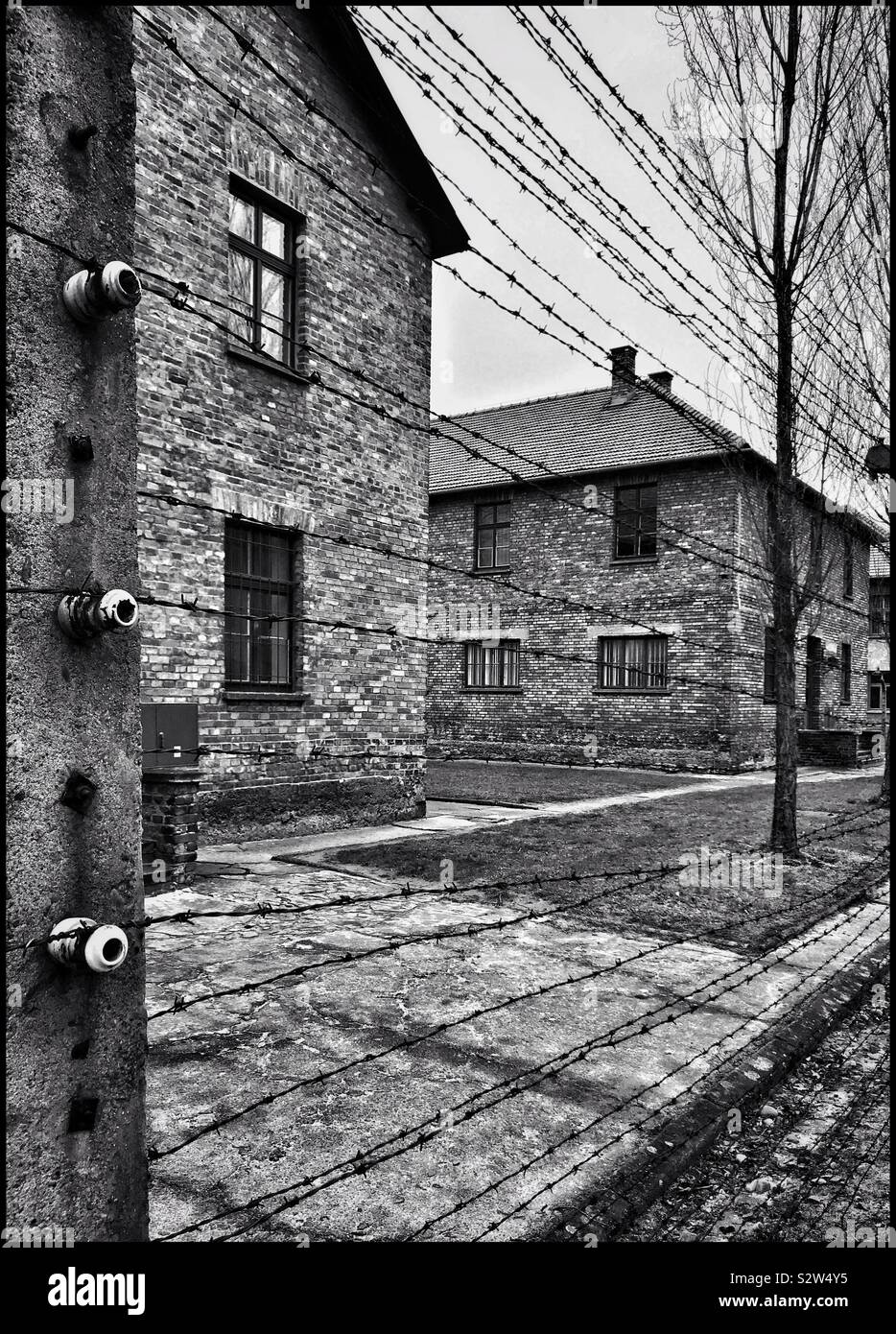 Una visualizzazione monocromatica di alcuni degli edifici al nazista di campo di concentramento di Auschwitz (nella città polacca di Oswiecim). Il elettrica e filo spinato scherma è chiaramente visibile. Foto © COLIN HOSKINS. Foto Stock