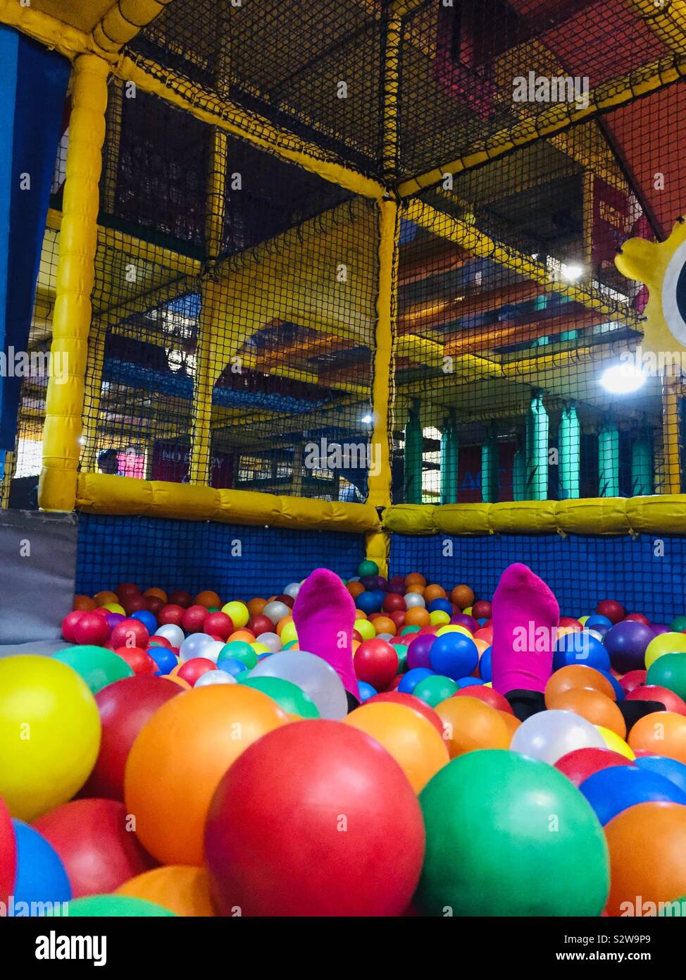 Donna di piedi con calze rosa mostrato in una sfera di softplay pool di multi colore sfere di plastica all'interno di un telaio di Softplay Foto Stock