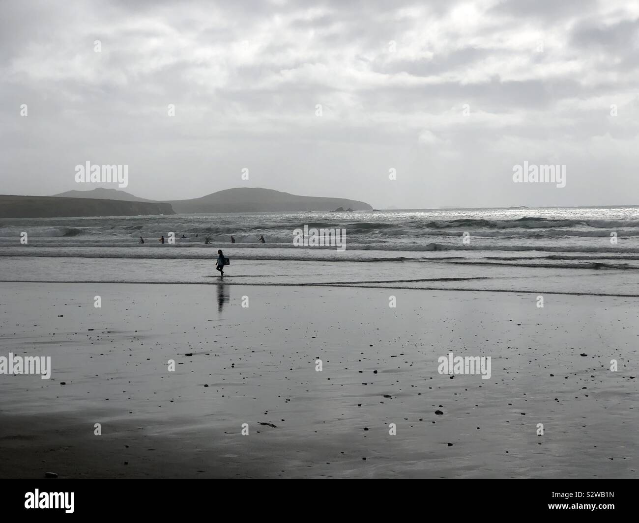 Surfers stagliano contro pioggia, nebbia e cielo tempestoso e high surf in spiaggia Whitesands Pembrokeshire, durante le tempeste e notevole luce argentea. Foto Stock