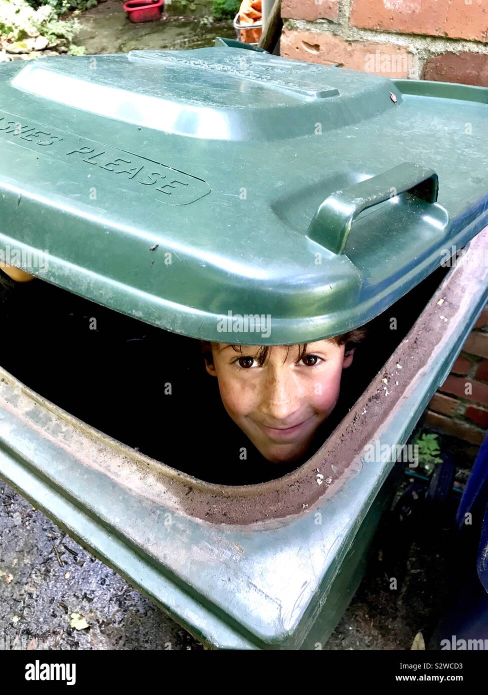 Un ragazzo si nasconde in un bidone con ruote. Foto Stock