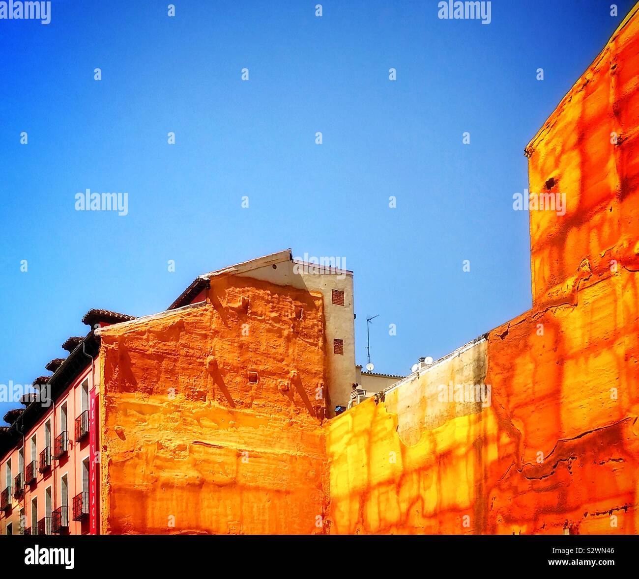 Ondata di caldo. Le pareti degli edifici adiacenti ad un vacante terreno edificabile sono rivestiti e sigillati con un giallo oro materiale di cemento e di irradiare calore nel sole luminoso in una giornata molto calda. - Immagine stock catturata con smartphone