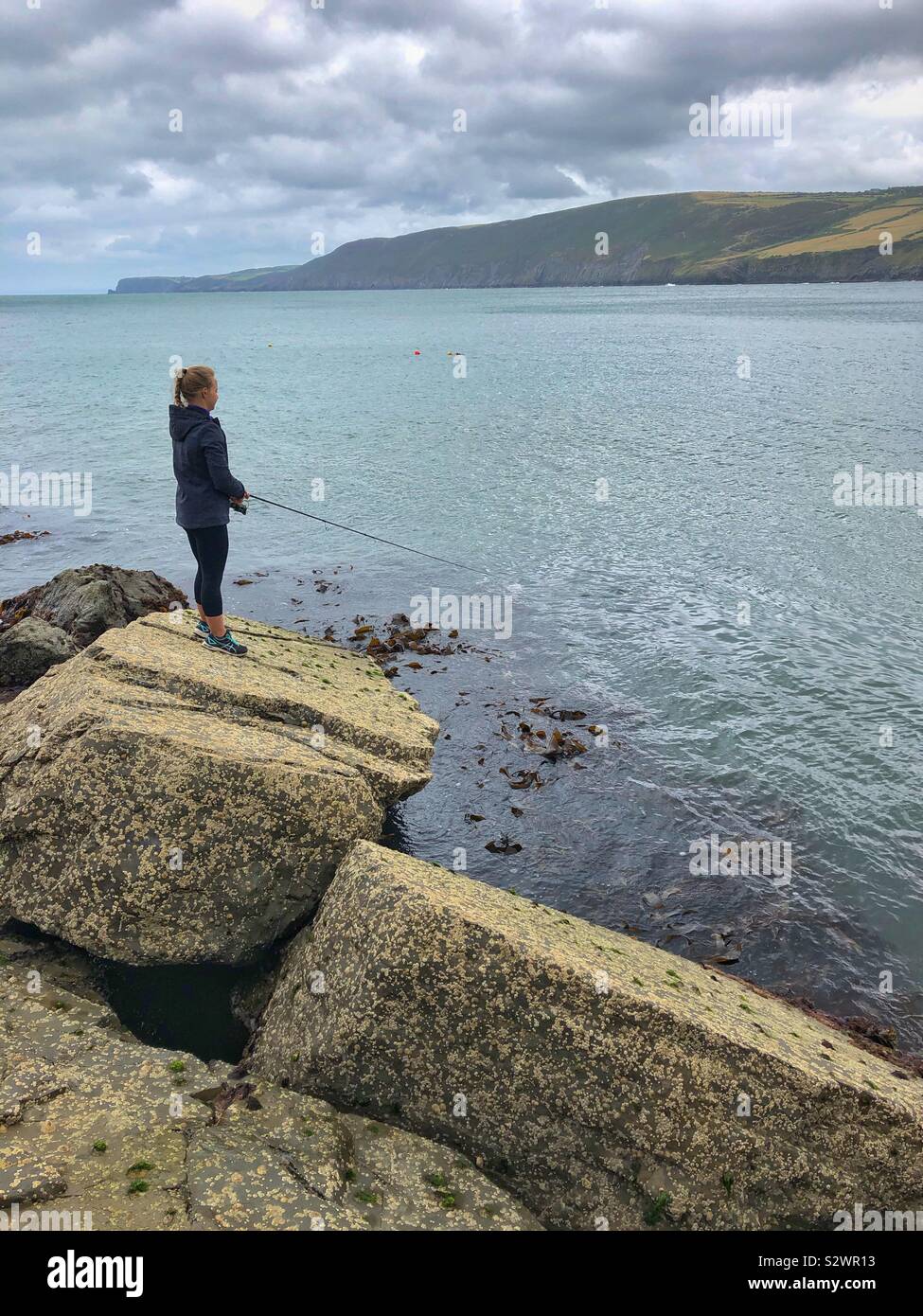 Giovane donna la pesca sulla costa gallese, Agosto. Foto Stock