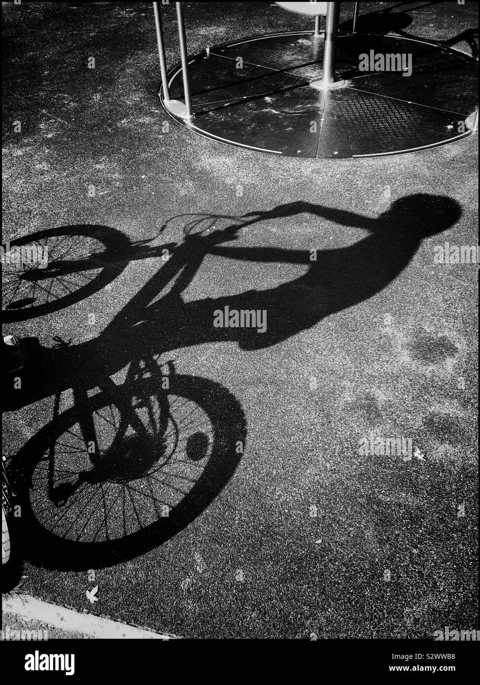 L'ombra di un ragazzo in sella alla sua bicicletta in un parco giochi. Il sole splendente ha creato un interessante ombra sul terreno. Foto © COLIN HOSKINS. Foto Stock