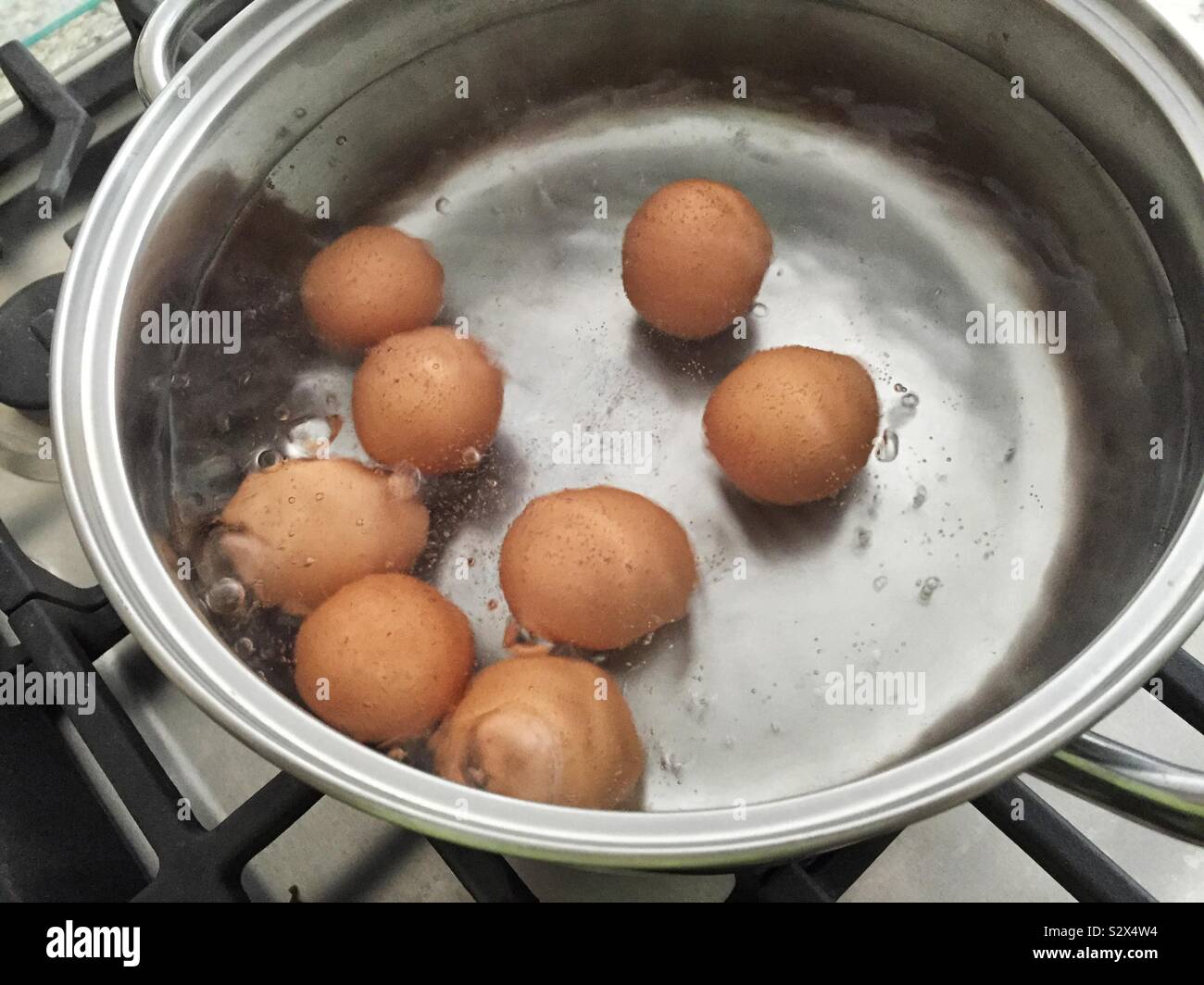 Otto marrone uova colorate sono bollitura in acqua in un recipiente in acciaio inossidabile Foto Stock