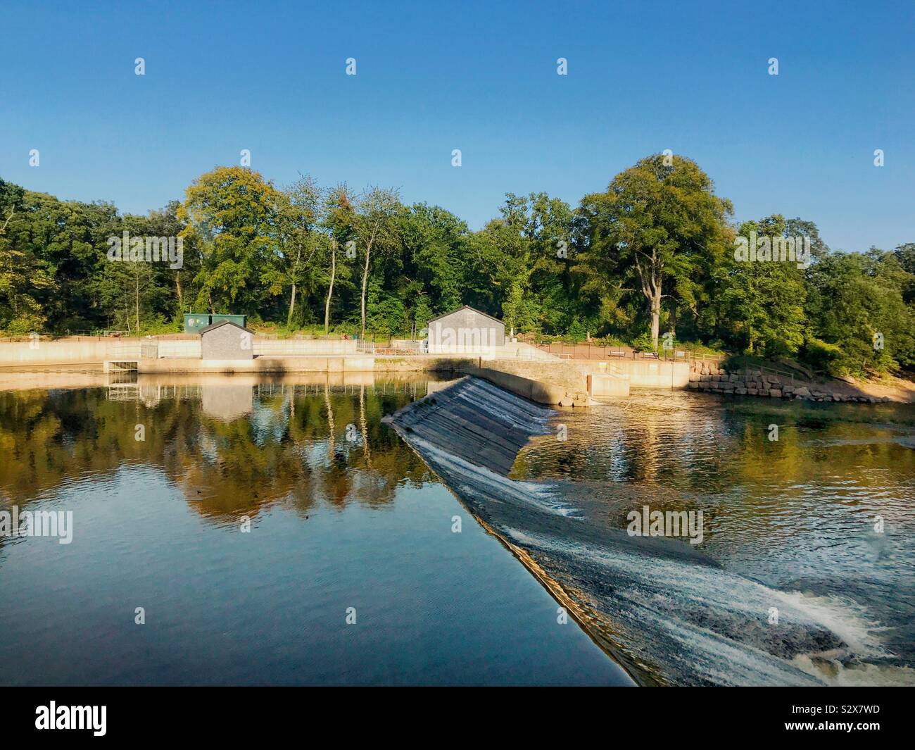 Ancora acqua sopra la diga sul fiume Taff a Radyr vicino a Cardiff. Sulla riva lontana sono gli edifici di schema idroelettrico Foto Stock