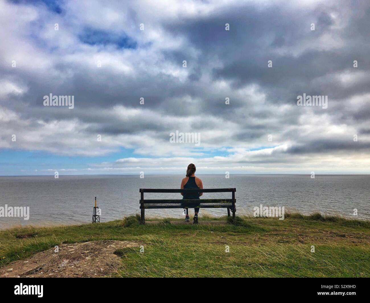 Giovane donna seduta su una panchina godendo della vista sul mare. - Immagine stock catturata con smartphone