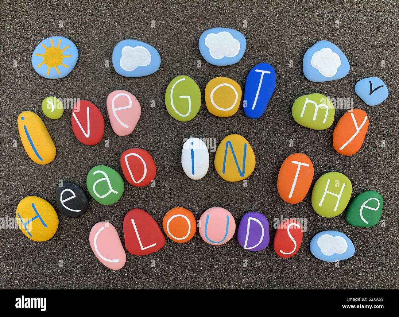 Ho la mia testa nelle nuvole, composizione creativa con pietre colorate su sabbia vulcanica nera - Immagine stock catturata con smartphone