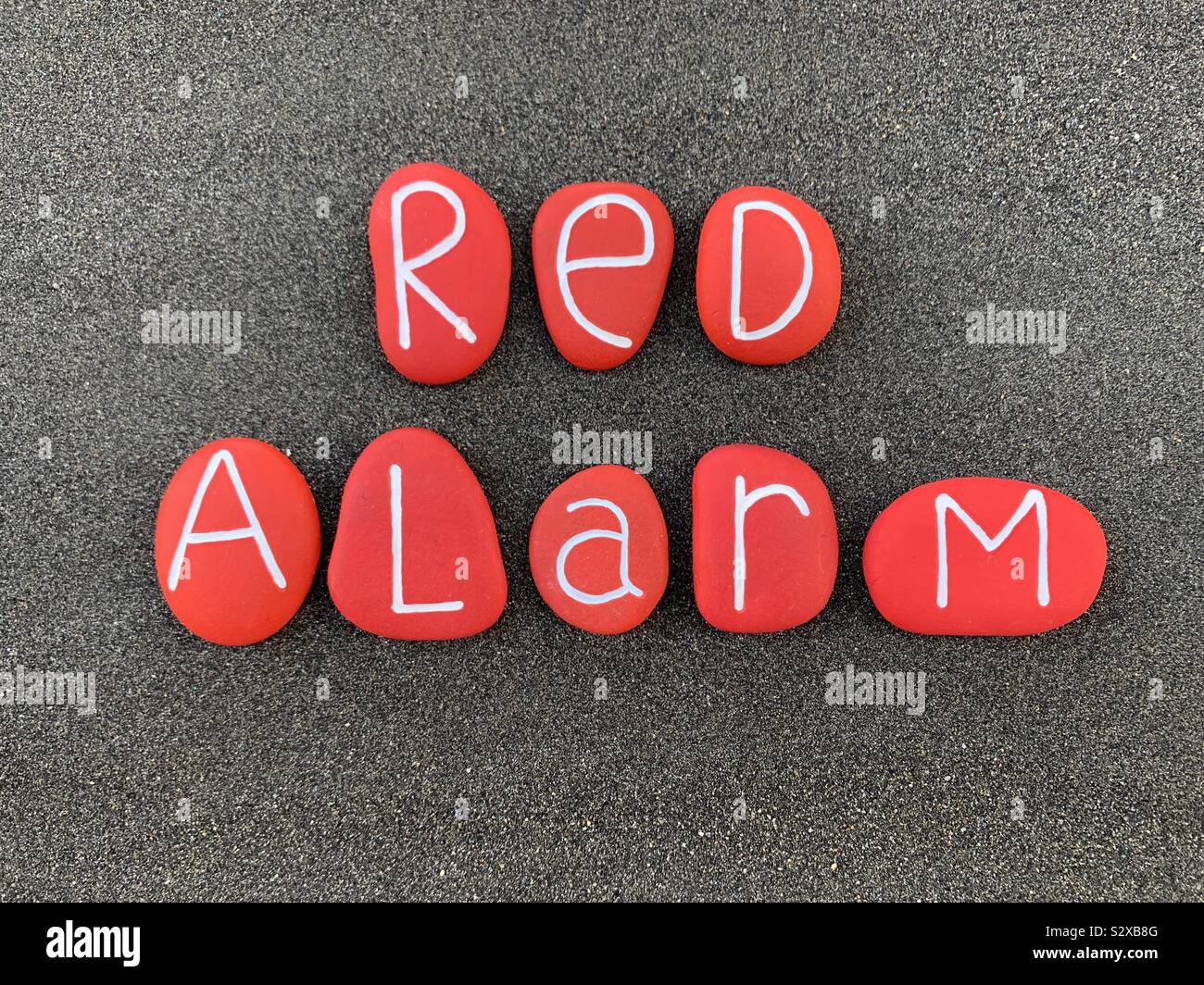 Allarme rosso composta di testo rosso con pietre colorate sulla sabbia nera vulcanica Foto Stock