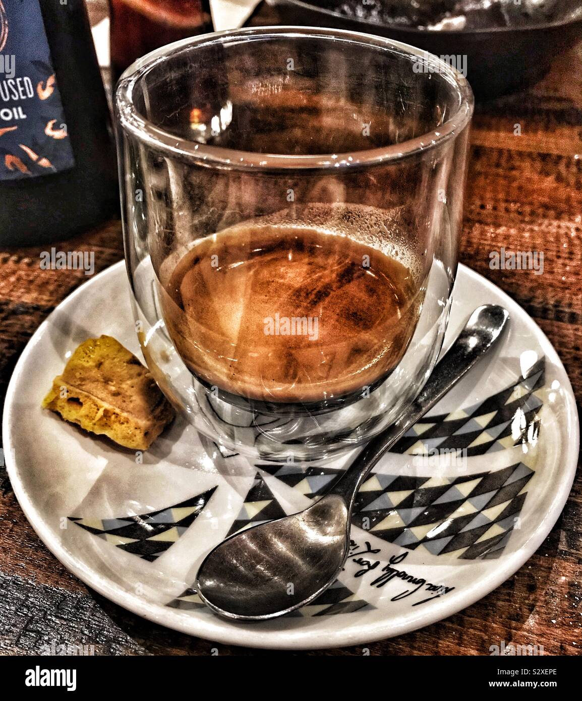Doppio Espresso in doppia parete in vetro su un piattino modellato con un favo di miele biscotti e cucchiaio Foto Stock