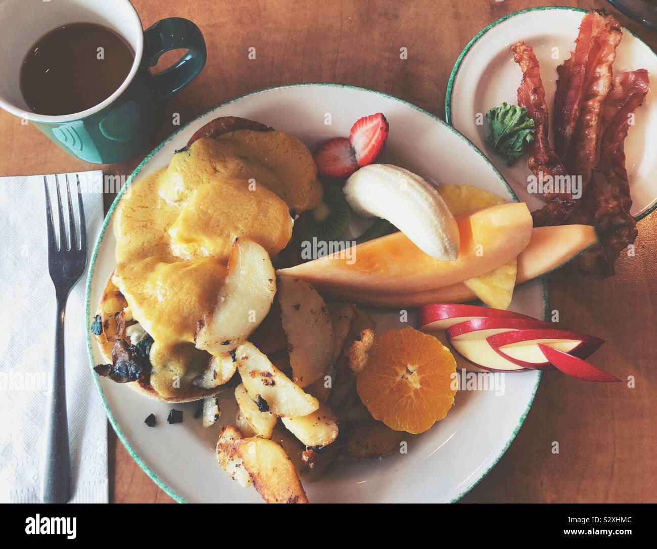 Uova Benedict con home patatine, frutta fresca, lato di pancetta e caffè Foto Stock