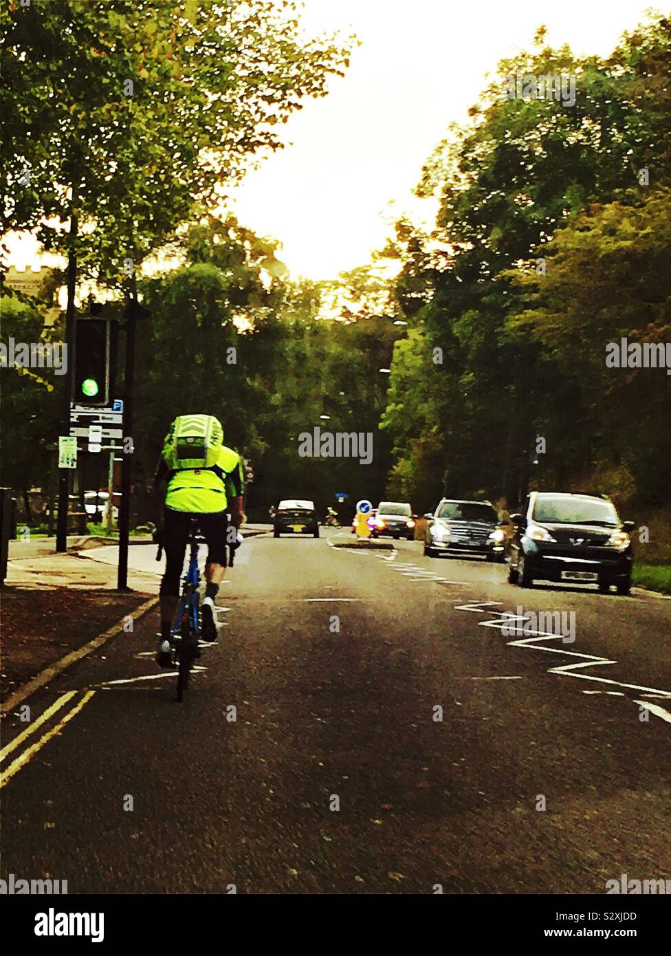 Un ciclista con alta visibilità abbigliamento, su una strada molto trafficata con alberi Foto Stock