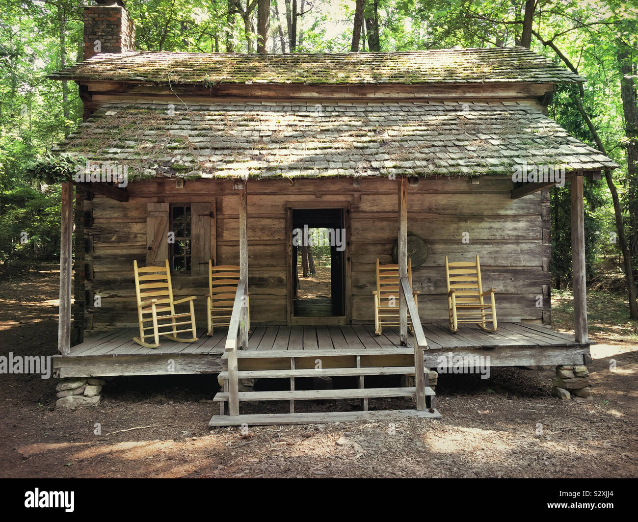 Vuoto in legno Sedie a dondolo sul portico anteriore di una vecchia casa di registro nei boschi. Questo log house è stato costruito in Pioneer Days of America durante il 1830s. Foto Stock