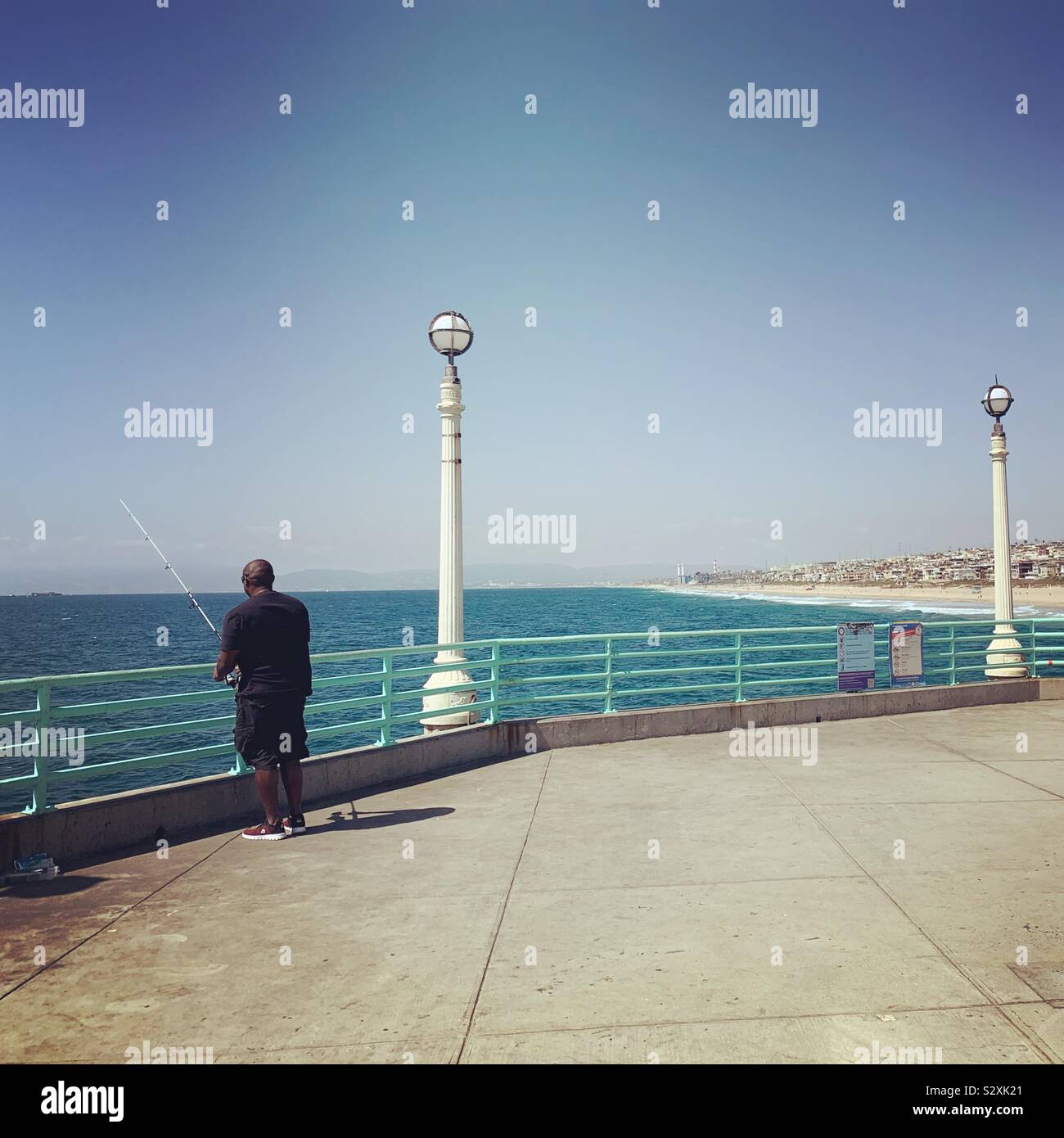 Un uomo pesca al largo di Manhattan Beach Pier, Manhattan Beach, California, Stati Uniti Foto Stock