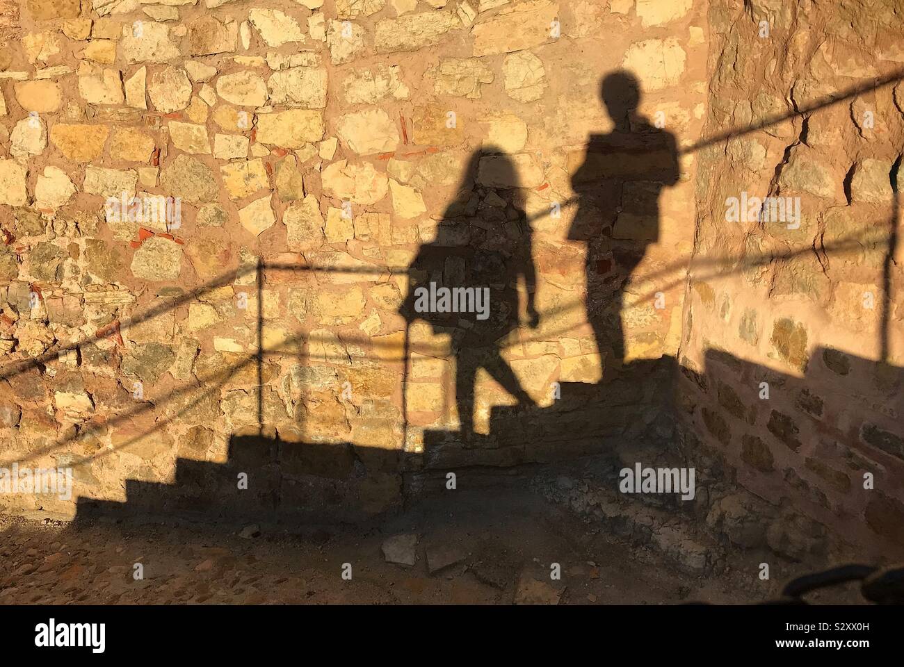 Passo nelle ombre....l'ombra di un giovane su gradini contro una parete di un castello medievale Foto Stock