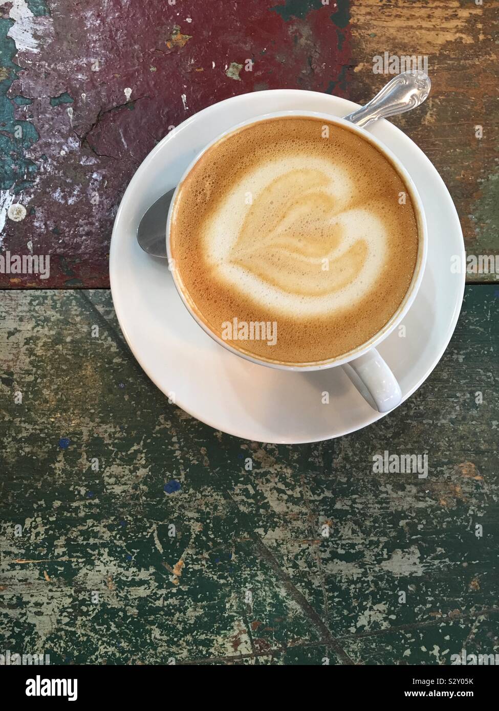 Schiumoso espresso con un cuore lattiginoso laici piana dall'alto verticale con copia spazio. Tazza bianca e il piattino e cucchiaio. - Immagine stock catturata con smartphone