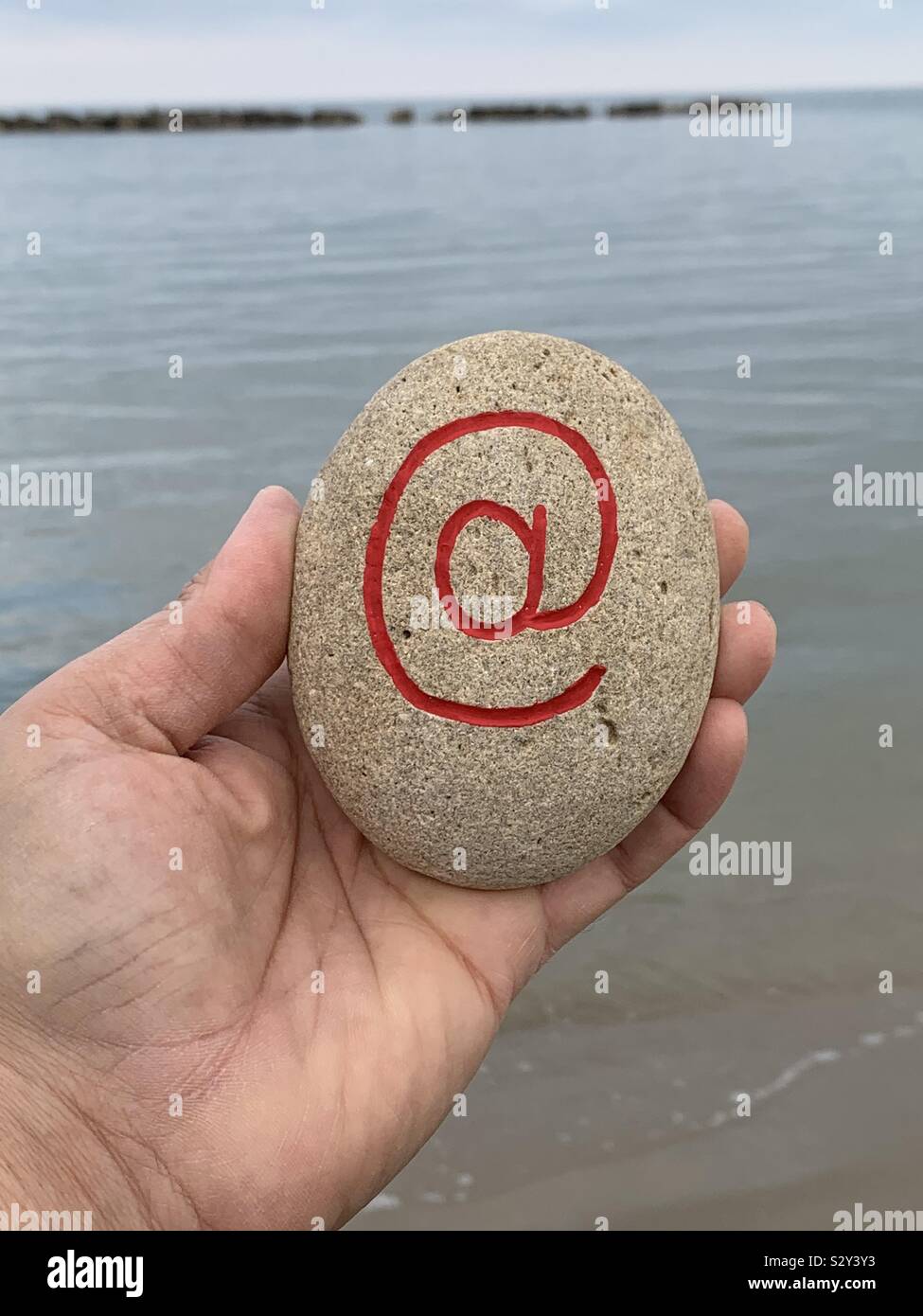 Et segno intagliato e dipinto di rosso su una pietra con lo sfondo del mare - Immagine stock catturata con smartphone