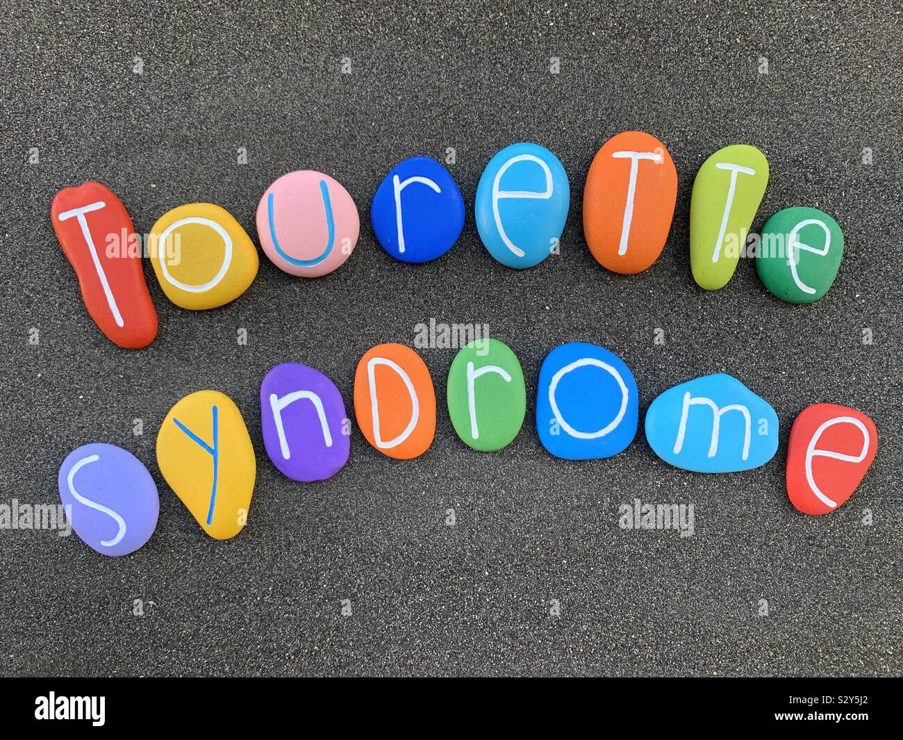 Sindrome di Tourette e creativo composto di testo con pietra multicolore lettere al di sopra di sabbia nera vulcanica - Immagine stock catturata con smartphone