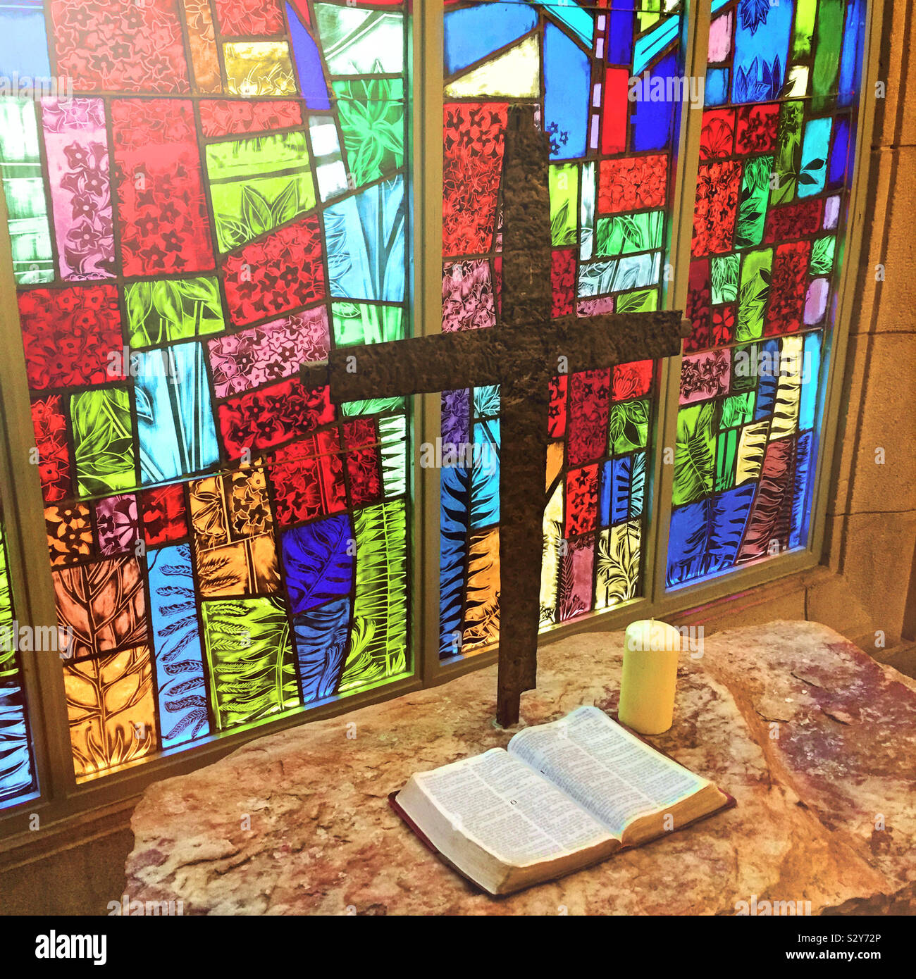 Coloratissima vetrata di illuminazione di una tabella in una chiesa che ha una croce religiosa e una Bibbia aperta su di esso. Foto Stock