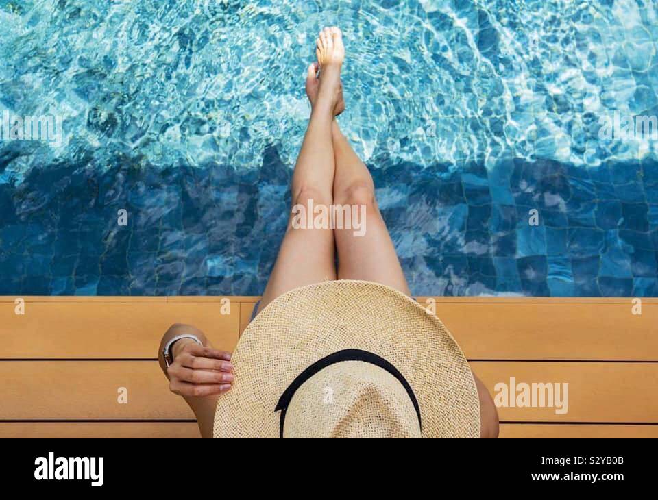 Guardando verso il basso in corrispondenza di una ragazza sedeva presso la piscina in una giornata di sole indossando un cappello Foto Stock