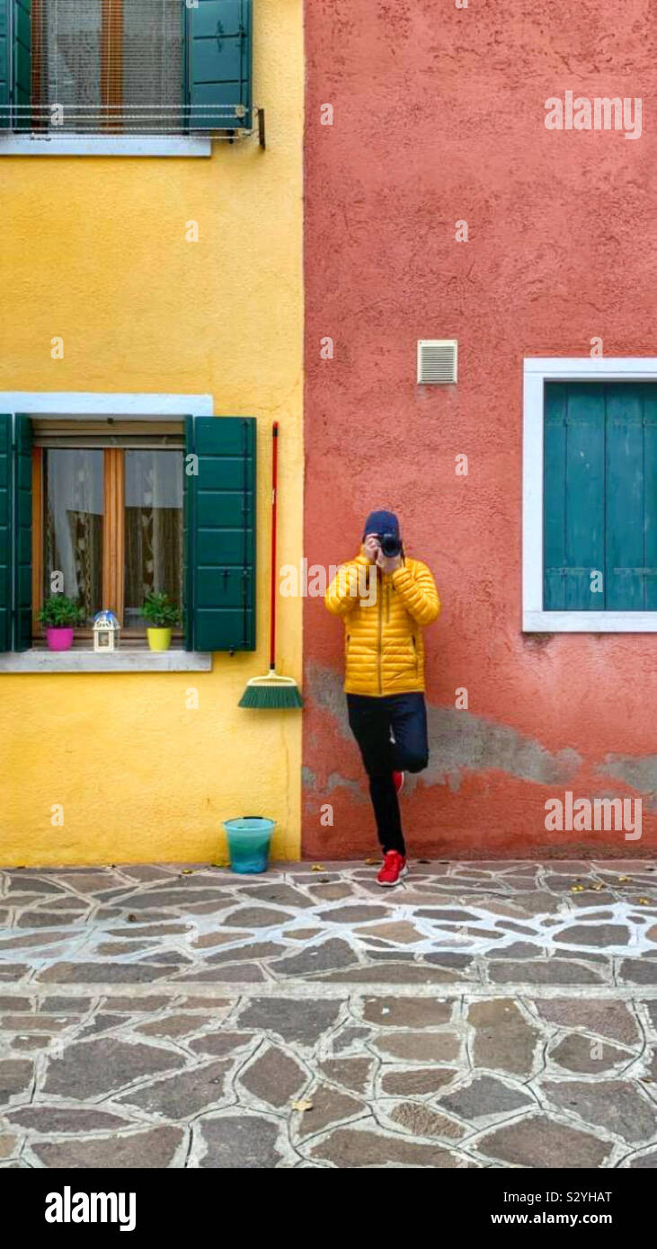 Fotografo appoggiata contro due case vivacemente colorate in Italia di Burano Foto Stock