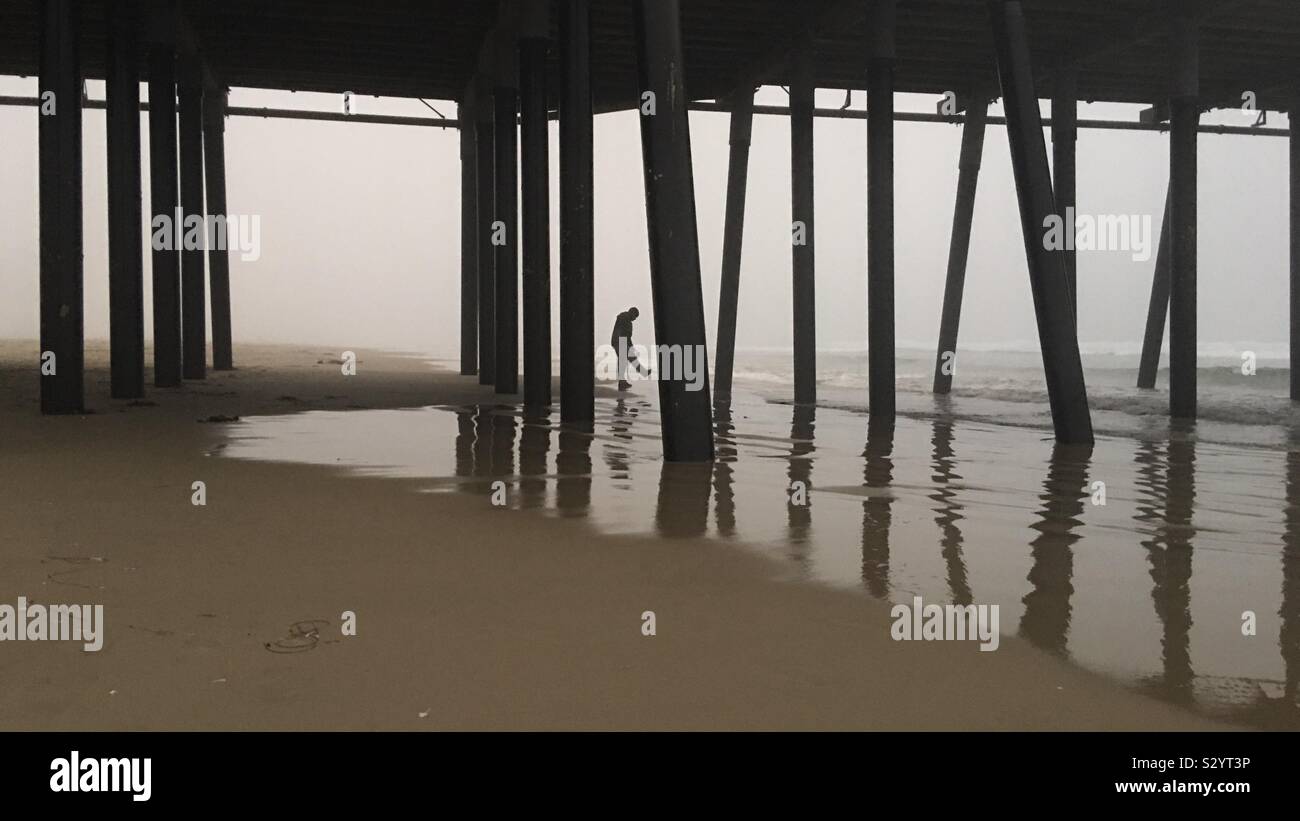 PISMO Beach, CA, OTT 2019: stagliano uomo calci al surf poco profondo sotto il molo su un nebbioso pomeriggio tardi Foto Stock