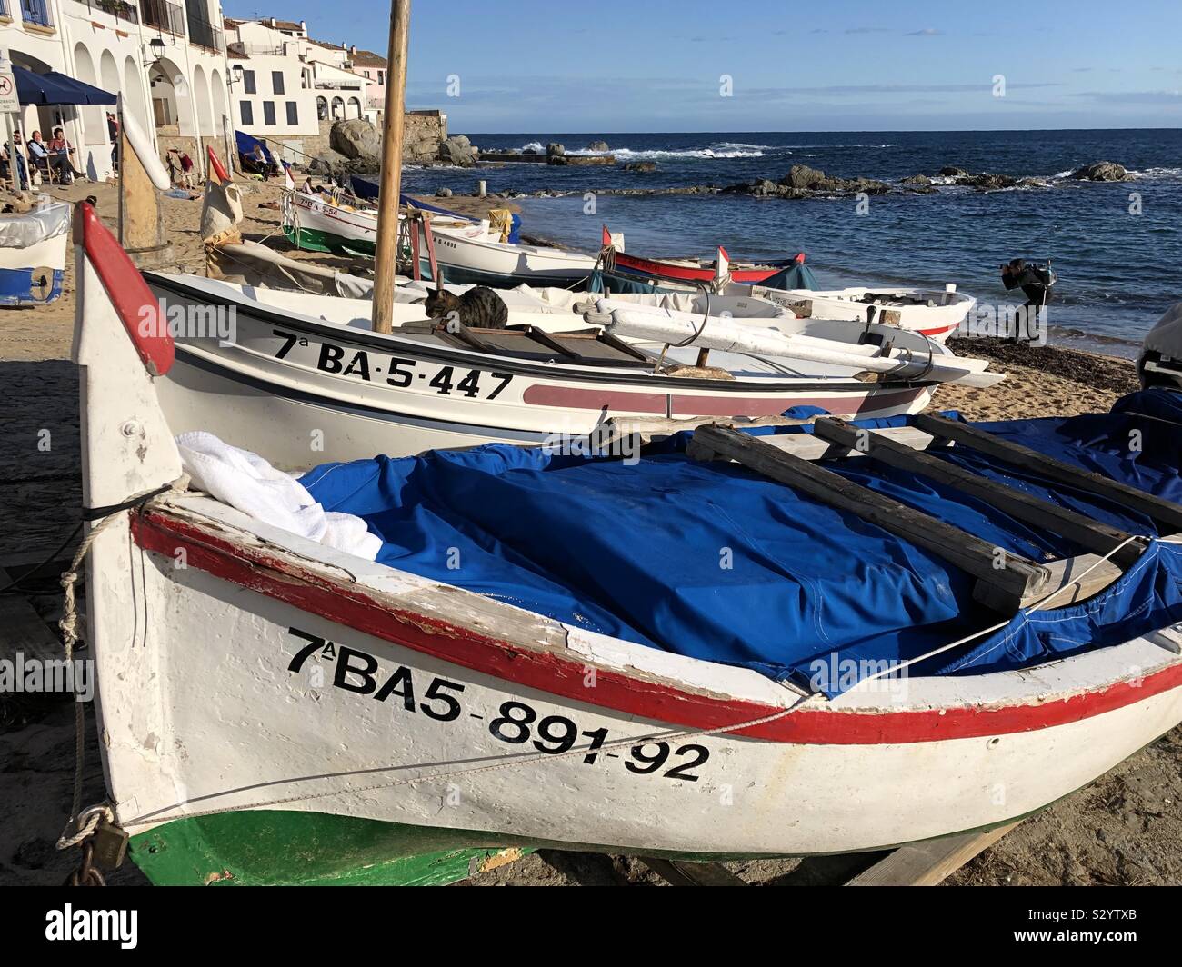 Tradizionali barche da pesca in appoggio sul Canadell spiaggia di Calella de Palafrugell in Costa Brava, Spagna, nel novembre sunshine. Un altro fotografo spotting una opportunità fotografica. Foto Stock