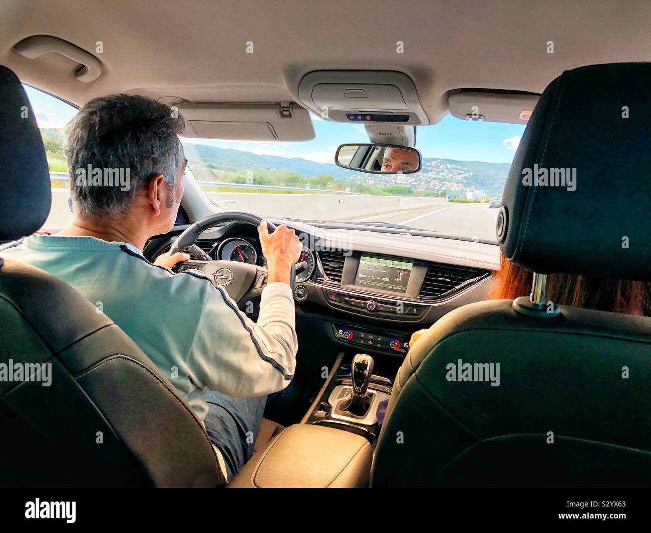 Un uomo alla guida di una auto a noleggio su una autostrada nel nord della Spagna in una giornata di sole con una luce calda come si vede dalla parte posteriore del sedile passeggero. - Immagine stock catturata con smartphone Un uomo alla guida di una auto a noleggio su una autostrada nel nord della Spagna in una giornata di sole con una luce calda come si vede dalla parte posteriore del sedile passeggero. - Immagine stock catturata con smartphone