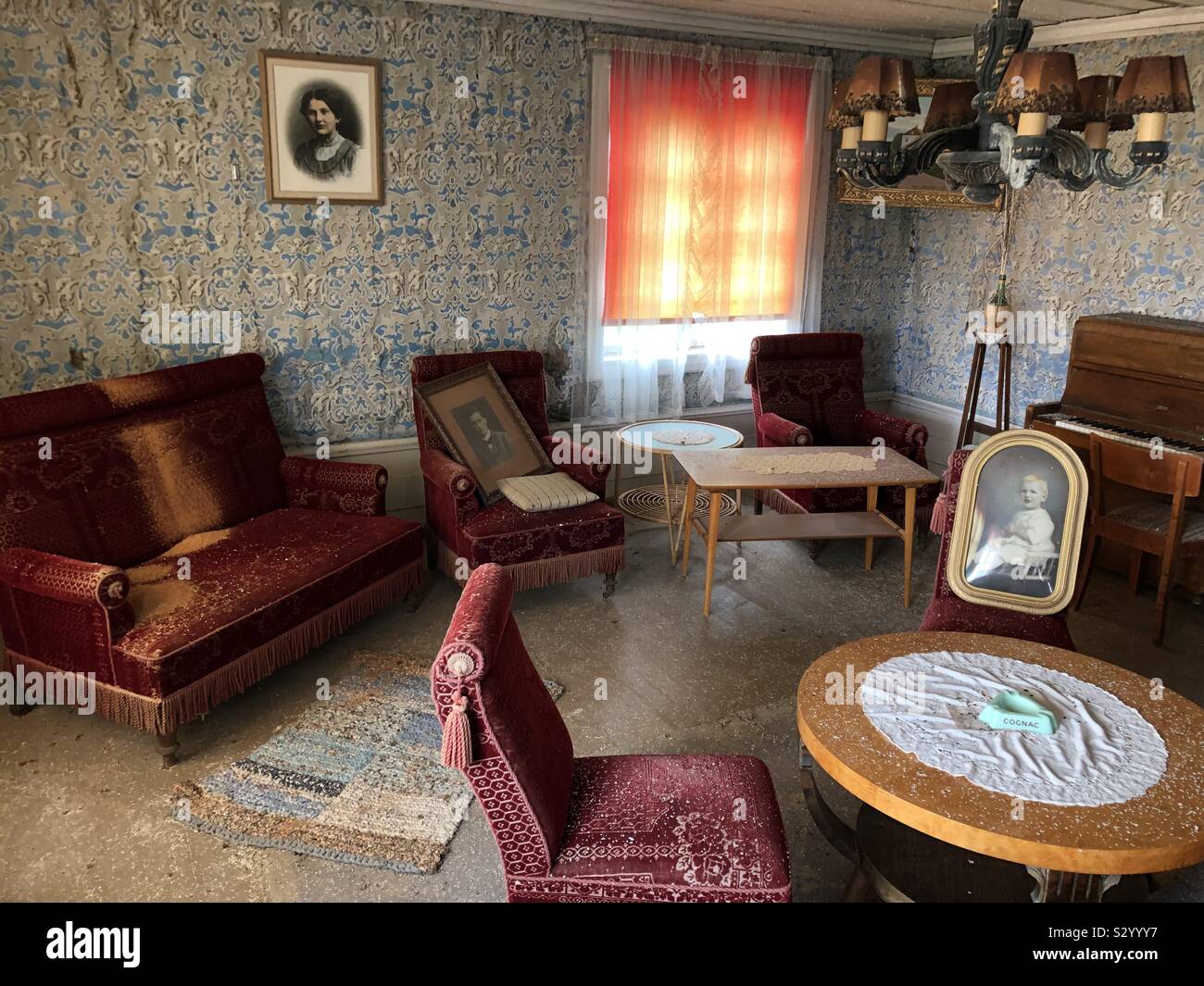 Decadendo salotto interno della vecchia fattoria abbandonata con stile vintage mobili, un pianoforte, incorniciato ritratti e pareti con carta da parati gregge. Foto Stock